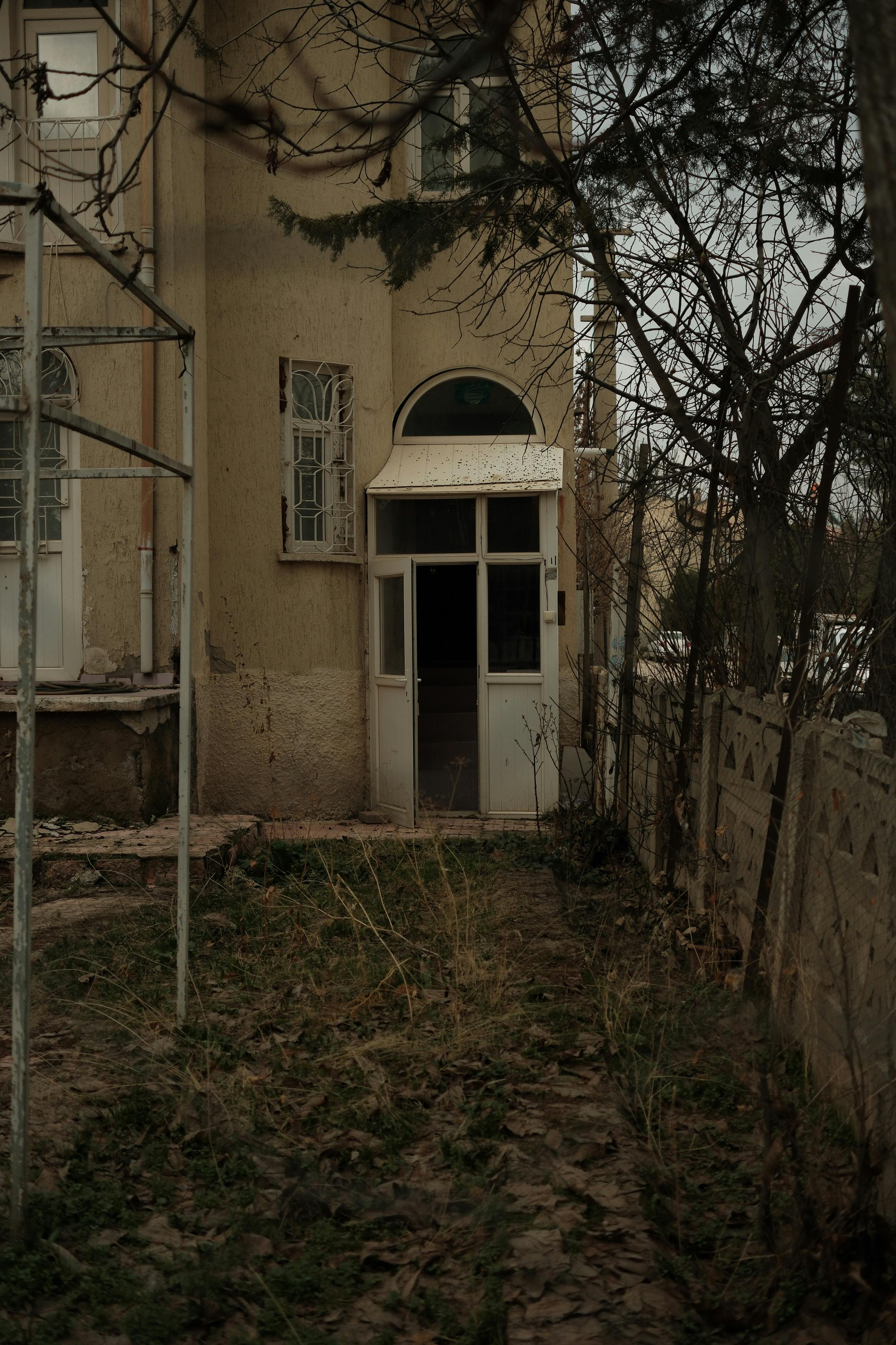 Kostenlos Ein unheimlicher Eingang zu einem alten, verlassenen Haus, umgeben von kahlen Bäumen. Stock-Foto