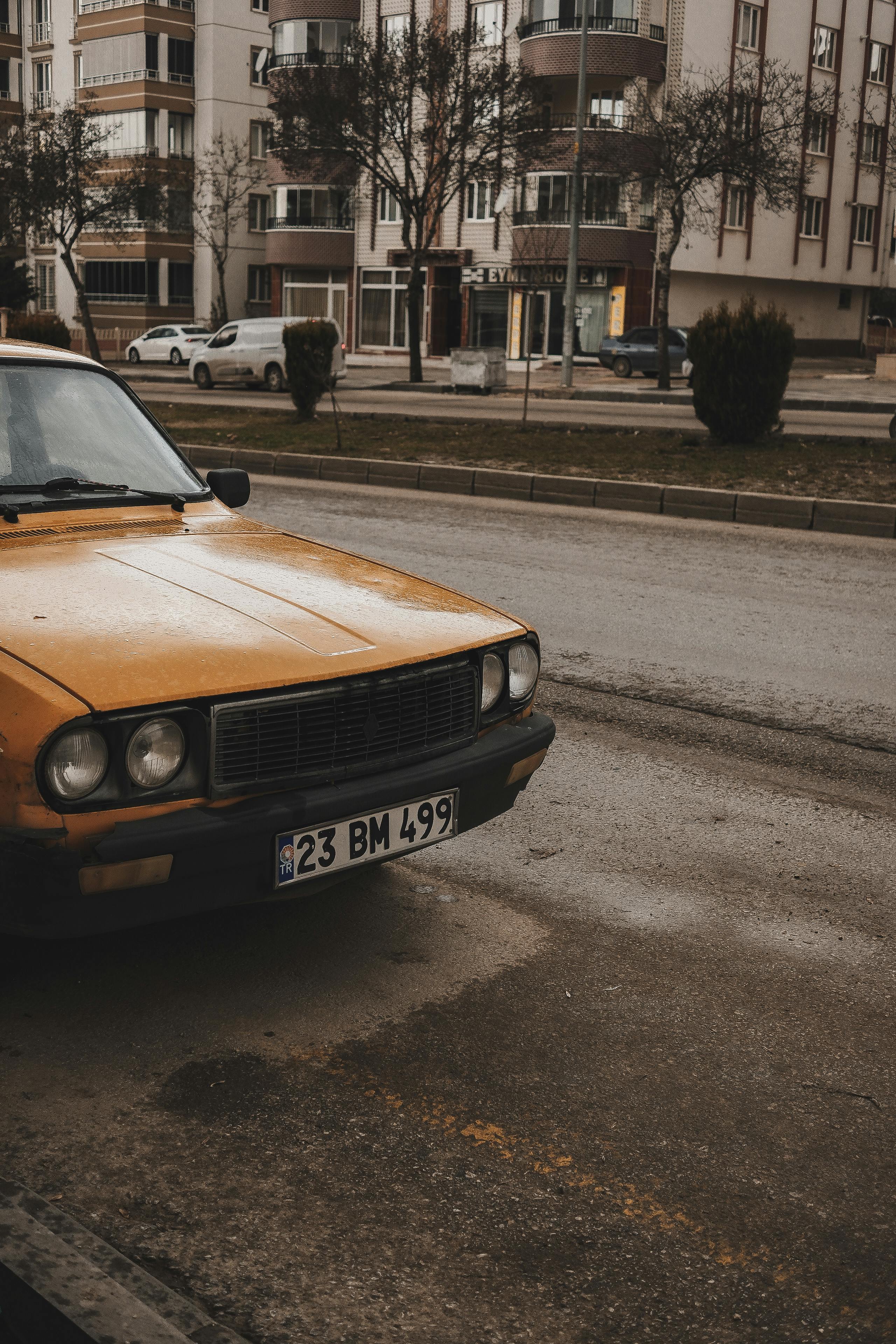 Bezpłatne Klasyczny żółty samochód zabytkowy zaparkowany na ulicy miasta na tle miejskich budynków. Zdjęcie z galerii