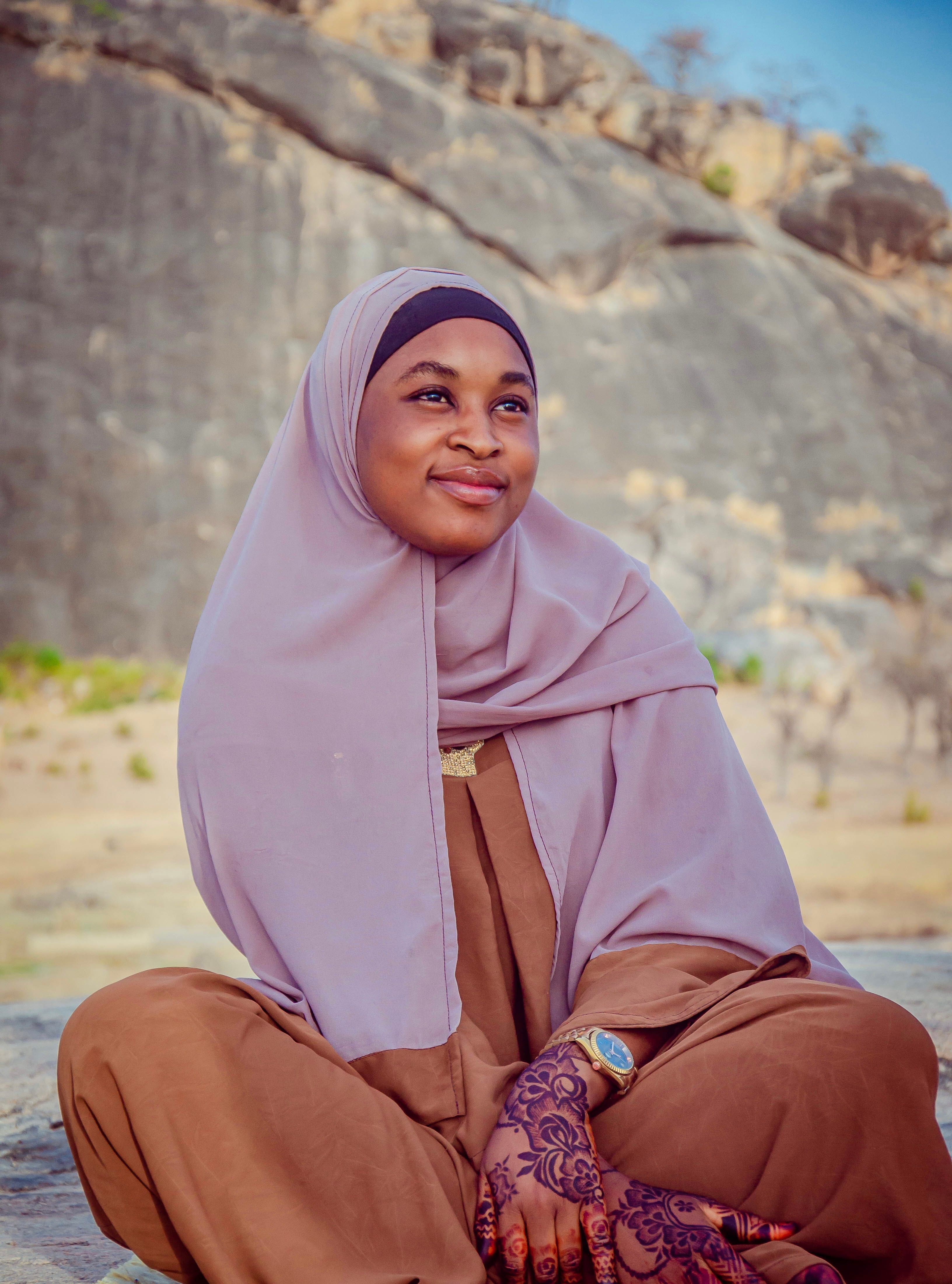 Outdoor portrait of a smiling woman in a hijab, surrounded by rugged rock formations.