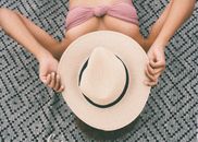 一位戴着草帽、身穿比基尼上衣的女人正晒着日光浴，拥抱夏日的气息