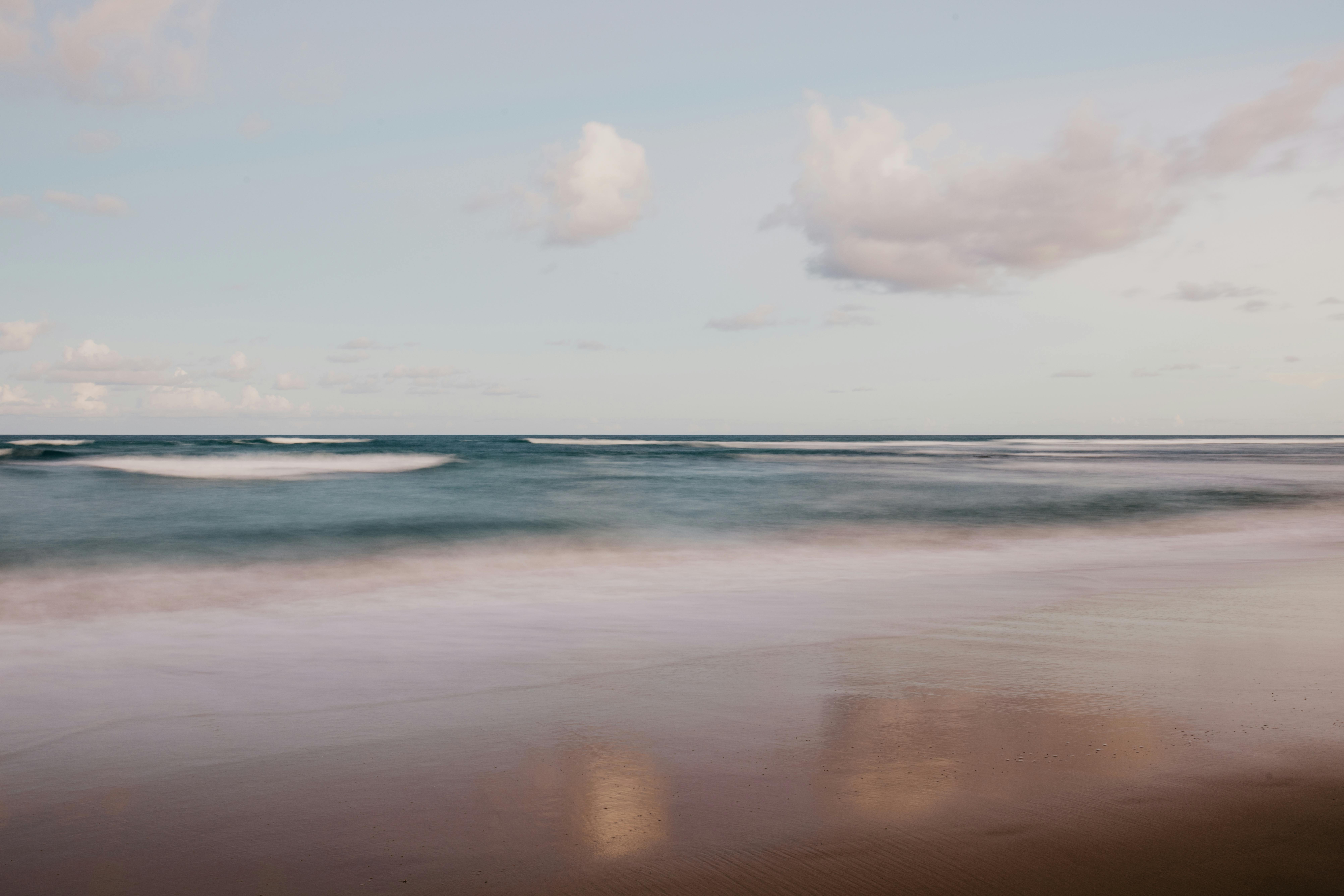 Bezpłatne Spokojne fale oceanu delikatnie obmywają brzeg pod zachmurzonym niebem. Zdjęcie z galerii