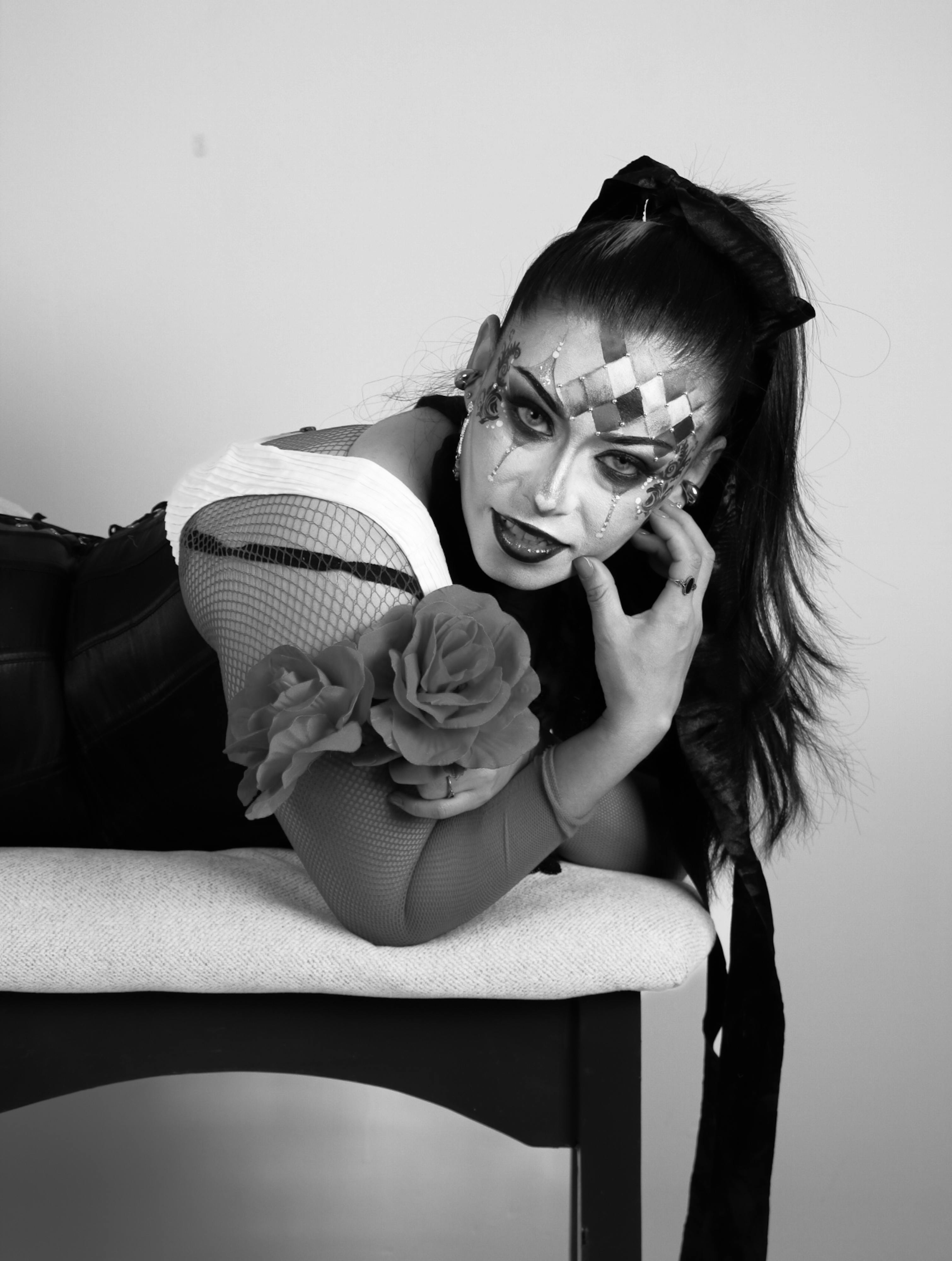 Bezpłatne Czarno-biały artystyczny portret kobiety z makijażem arlekina, leżącej na ławce. Zdjęcie z galerii