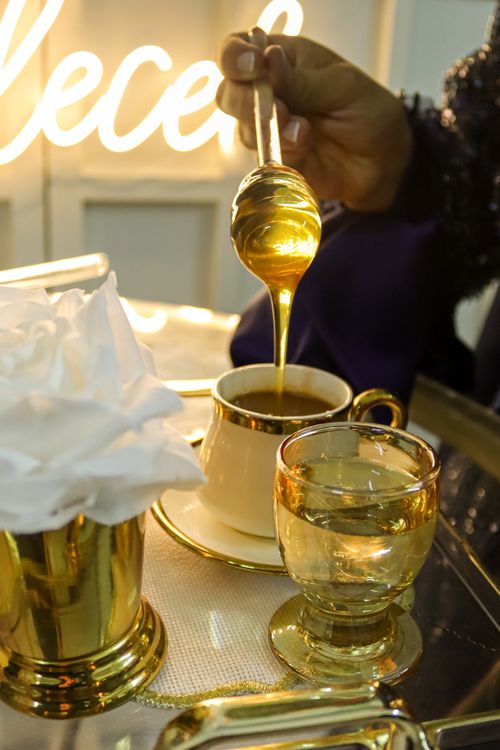Free Golden honey drizzling into a luxurious coffee cup on a reflective tray beside a glass of water. Stock Photo