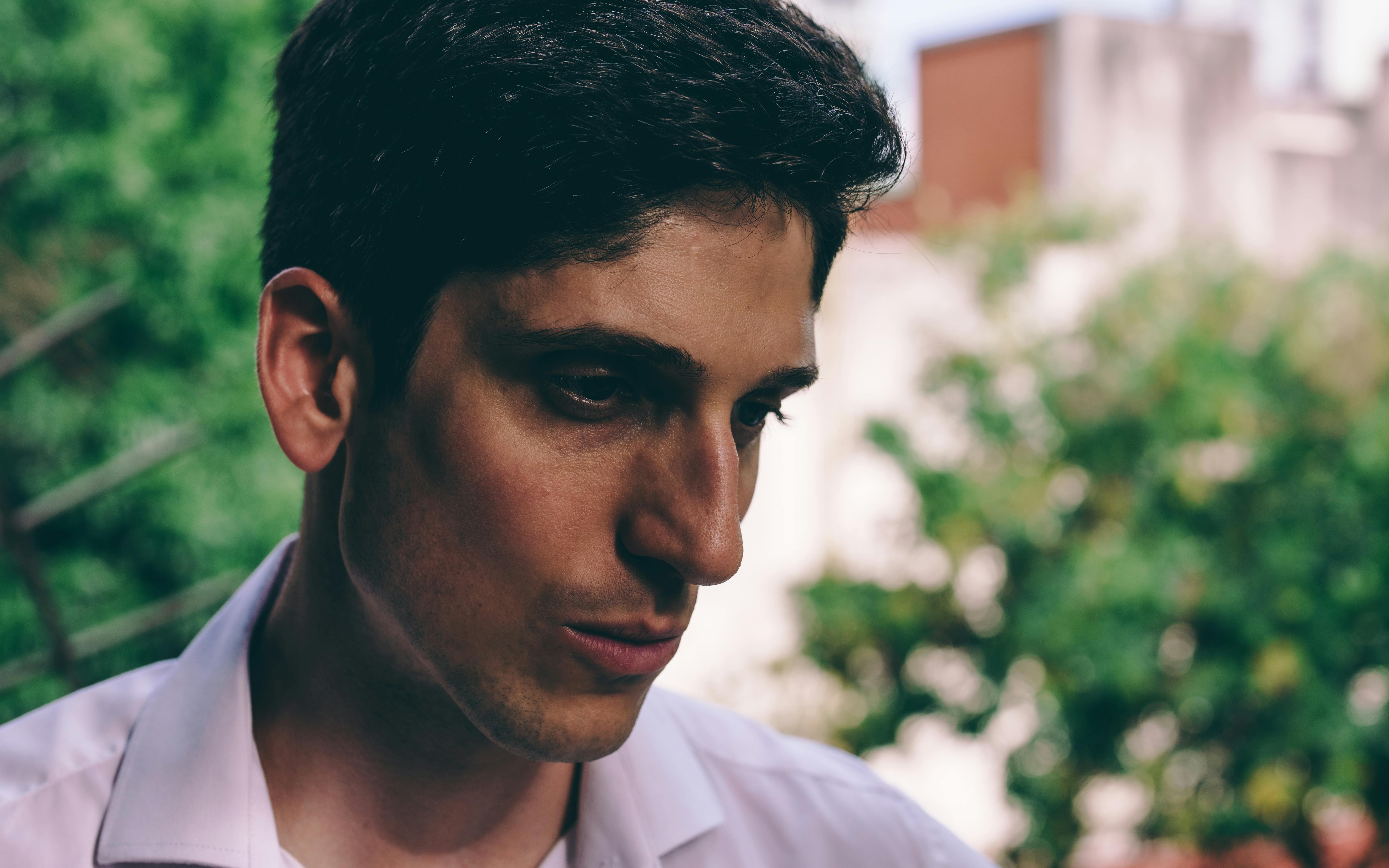 ฟรี ภาพถ่ายบุคคลของชายผู้ครุ่นคิดอยู่กลางแจ้ง โดยมีฉากหลังเป็นพืชพรรณสีเขียวที่พร่ามัว คลังภาพถ่าย