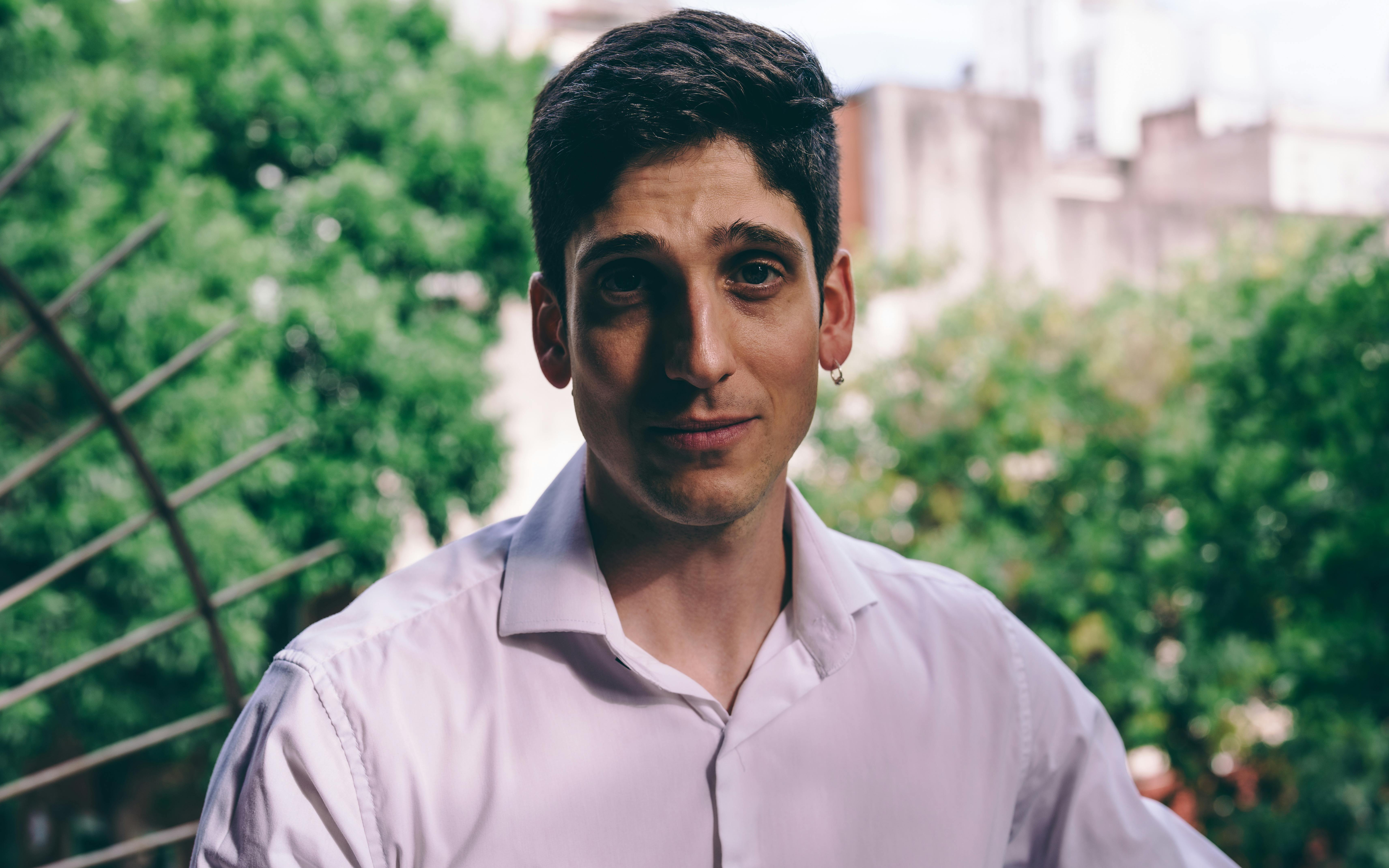 grátis Retrato de um jovem de camisa branca ao ar livre com fundo verde. Foto profissional