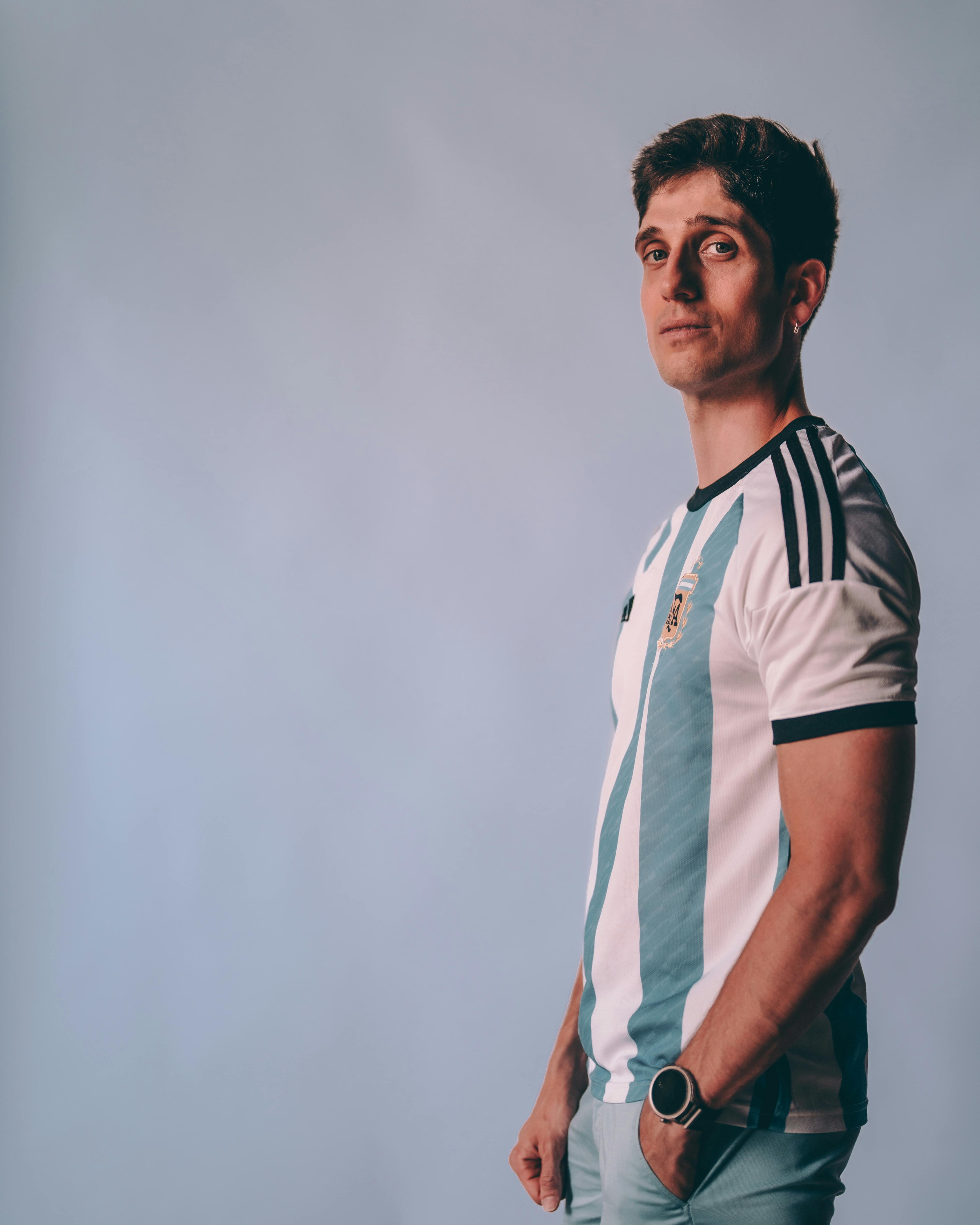 Bezpłatne Młody mężczyzna w koszulce argentyńskiej drużyny piłkarskiej pewnie pozuje w pomieszczeniu. Zdjęcie z galerii