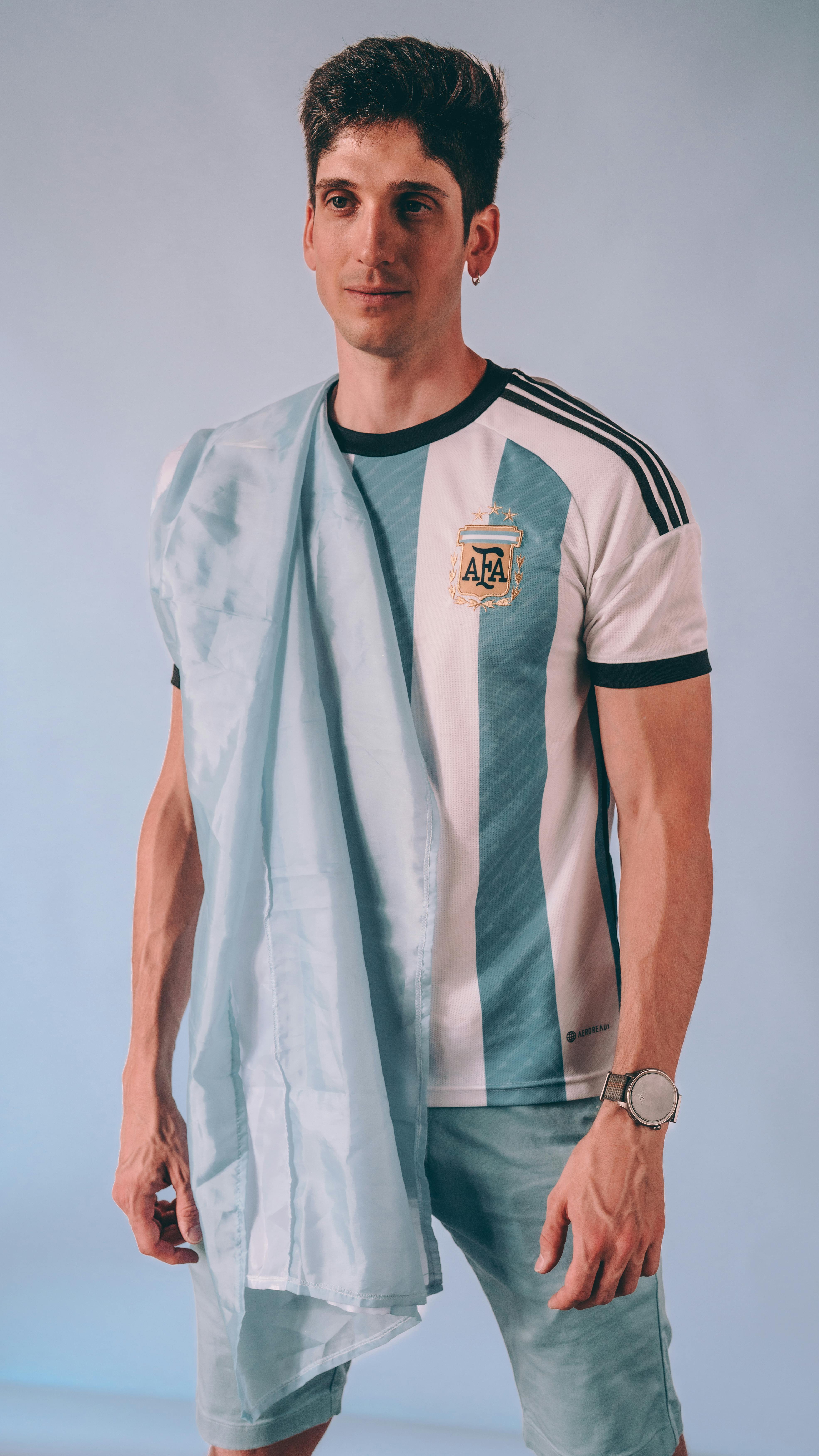 Portrait of young man in Argentina soccer jersey with national flag, indoor setting.