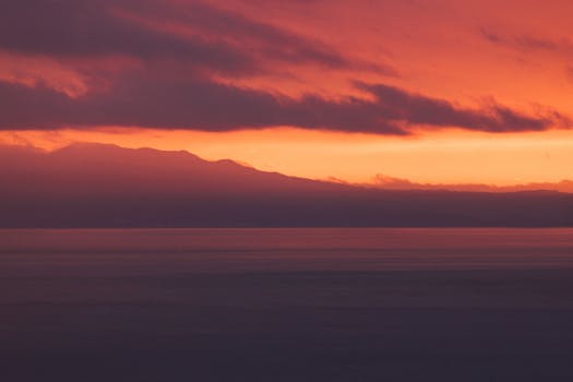 A vibrant, colorful sunset over a calm sea with silhouetted mountains in the background.