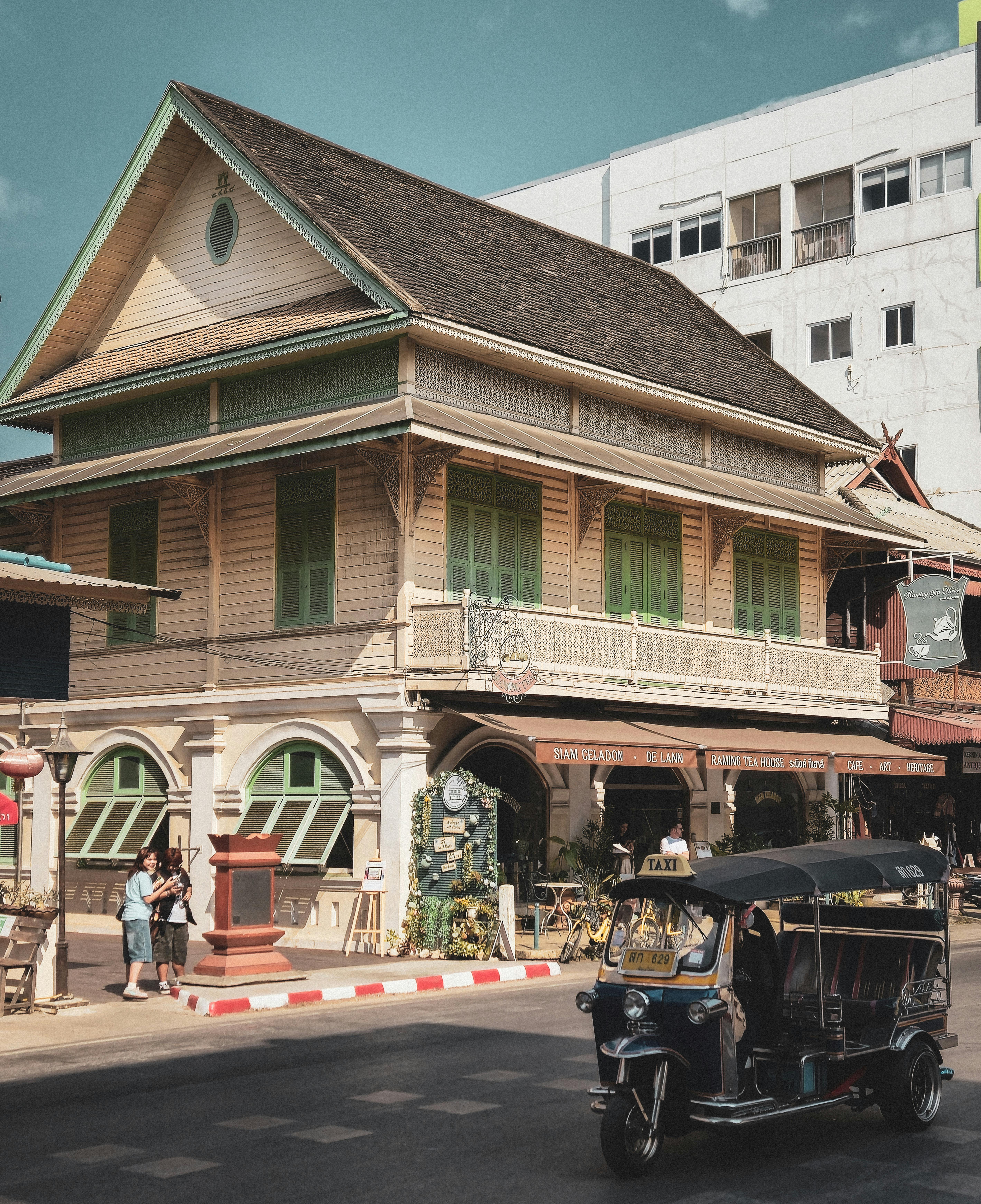 Gratis Sebuah rumah tradisional Thailand dengan tuk-tuk ikonik di dekatnya pada hari yang cerah. Foto Stok