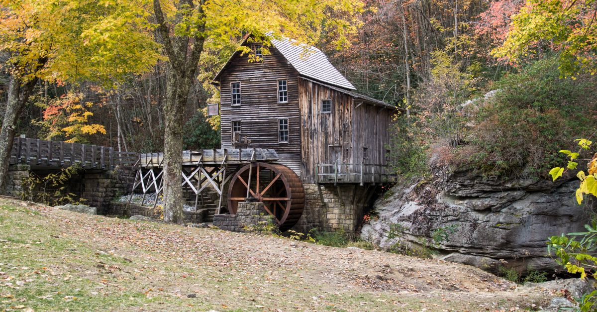 Charming wooden grist mill amidst autumn foliage, showcasing rustic architecture in a serene rural setting.