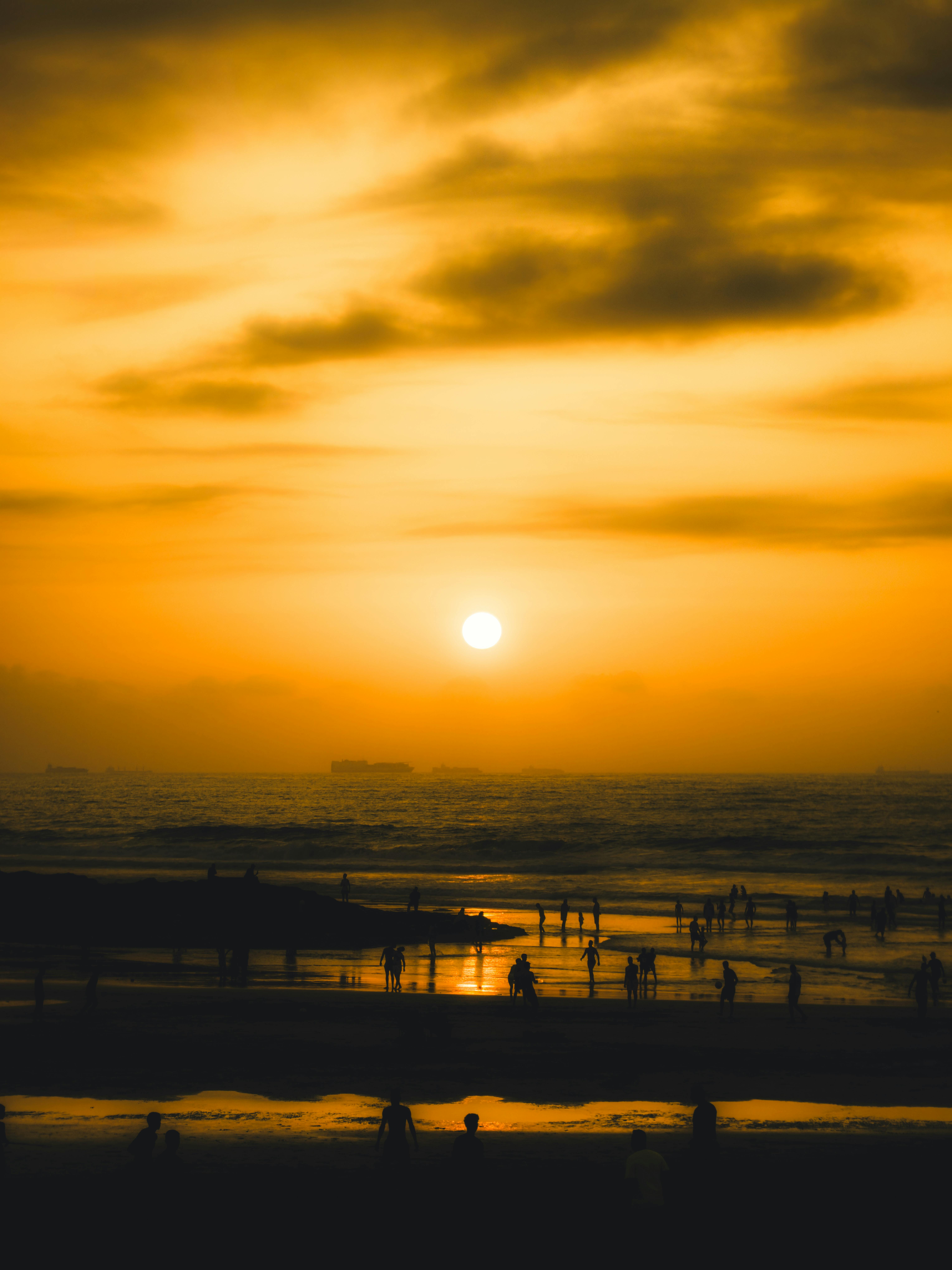 Free Golden sunset over a tranquil beach with silhouettes of people enjoying the evening light. Stock Photo