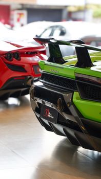 Close-up of luxury sports cars, green and red, showcased indoors, emphasizing sleek design.