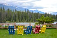 Vibrant Adirondack chairs facing a serene lake with mountain backdrop, perfect for relaxation.