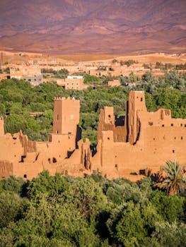 Explore the ancient mud brick architecture of a kasbah in Kalaat M'Gouna, surrounded by lush greenery.
