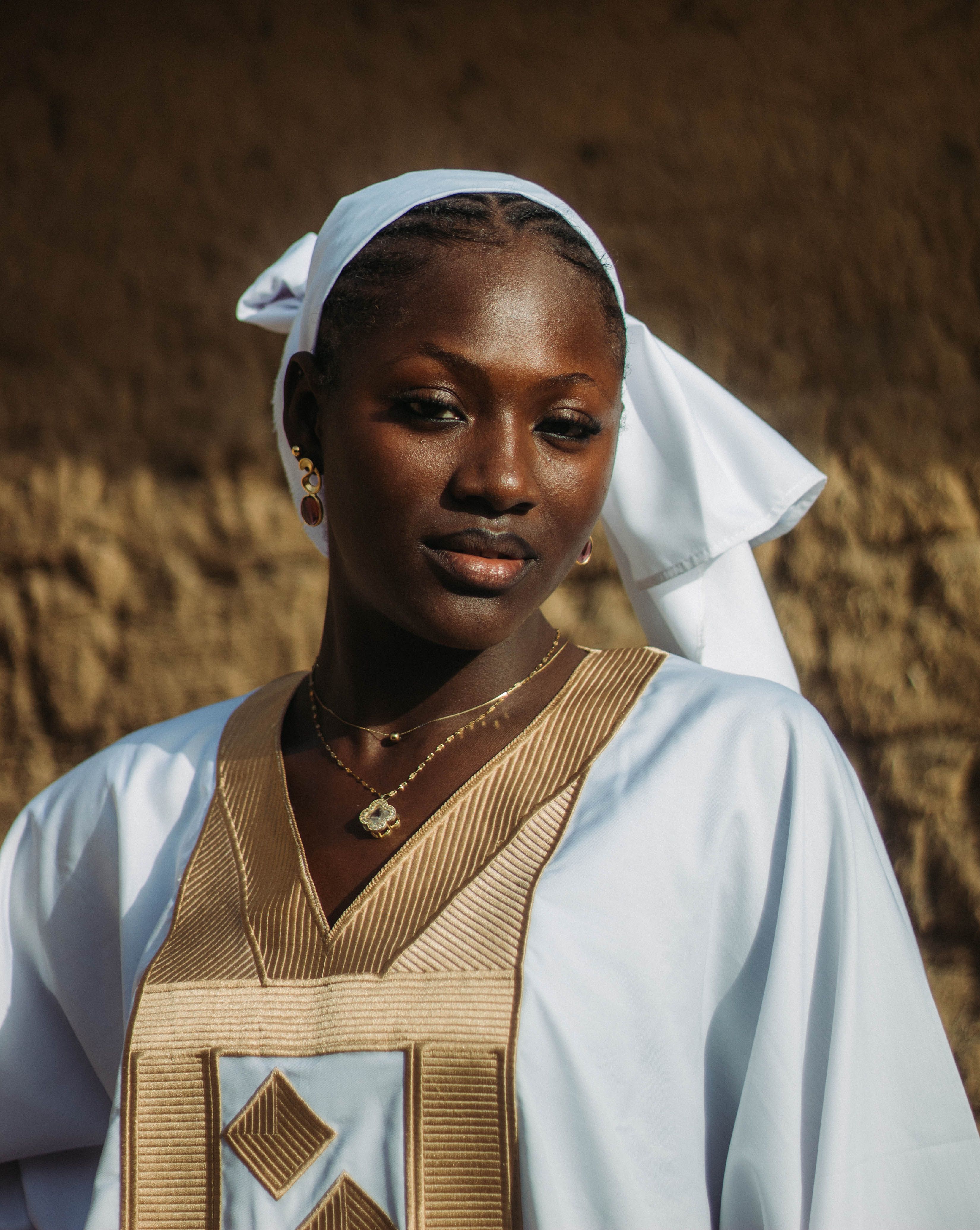 Portrait of a woman wearing traditional clothing, white headscarf, and gold jewelry.