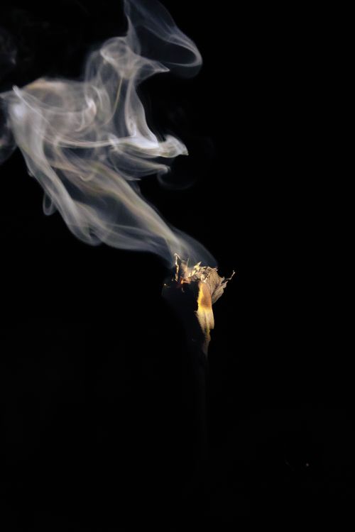 Free Dramatic image of smoke rising from a burning herb stick against a dark background. Stock Photo