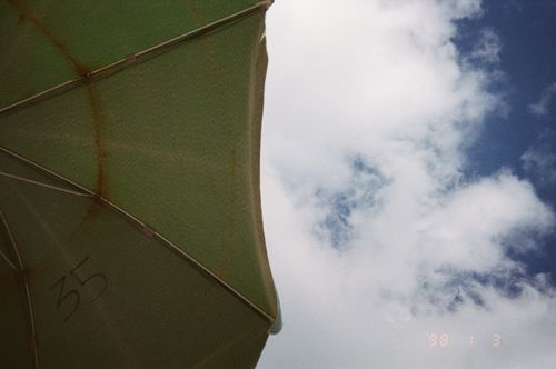 Free Partial view of a green beach umbrella with a cloudy blue sky. Stock Photo