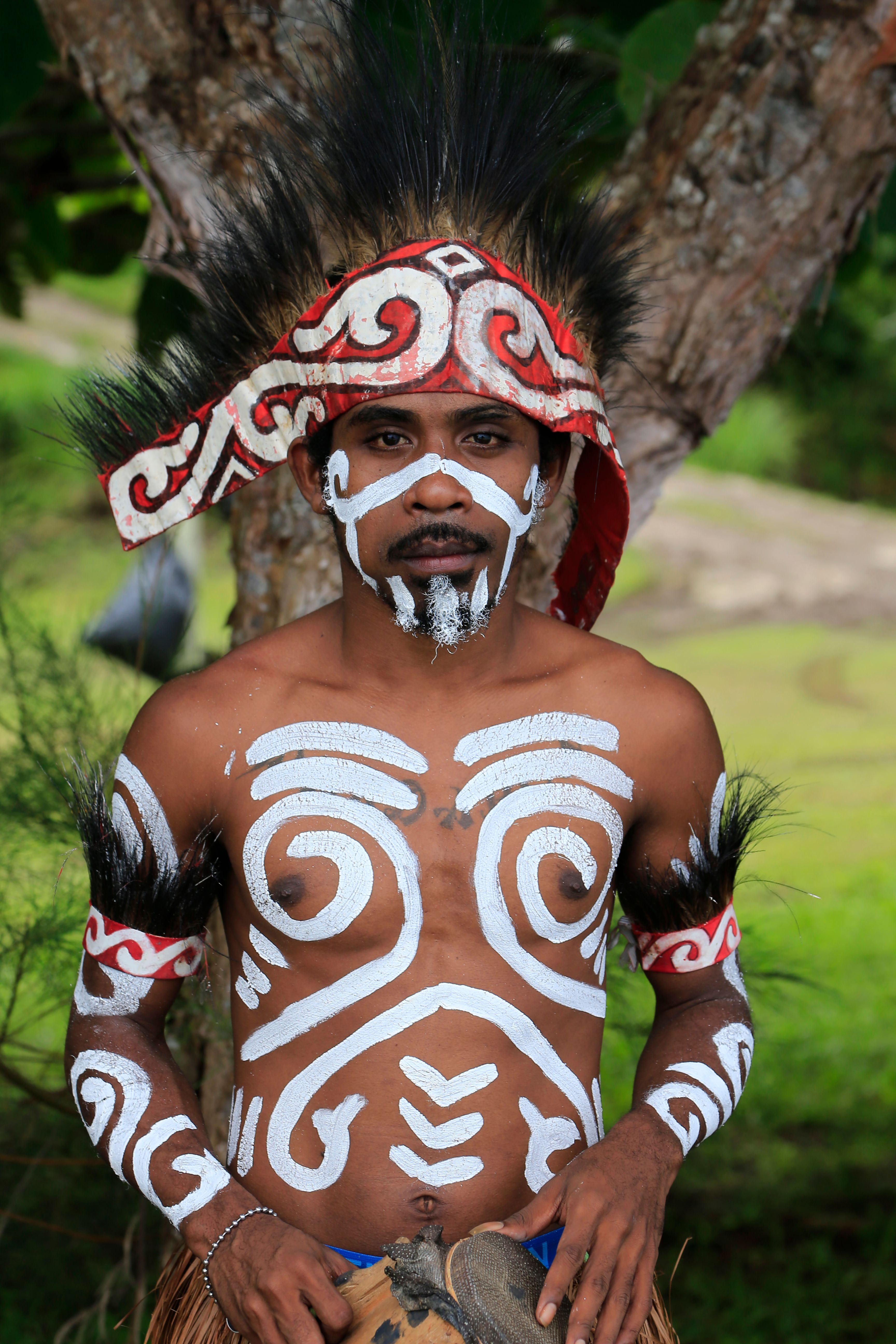 Man in traditional Papua New Guinean tribal attire with body paint and decorative headdress outdoors.