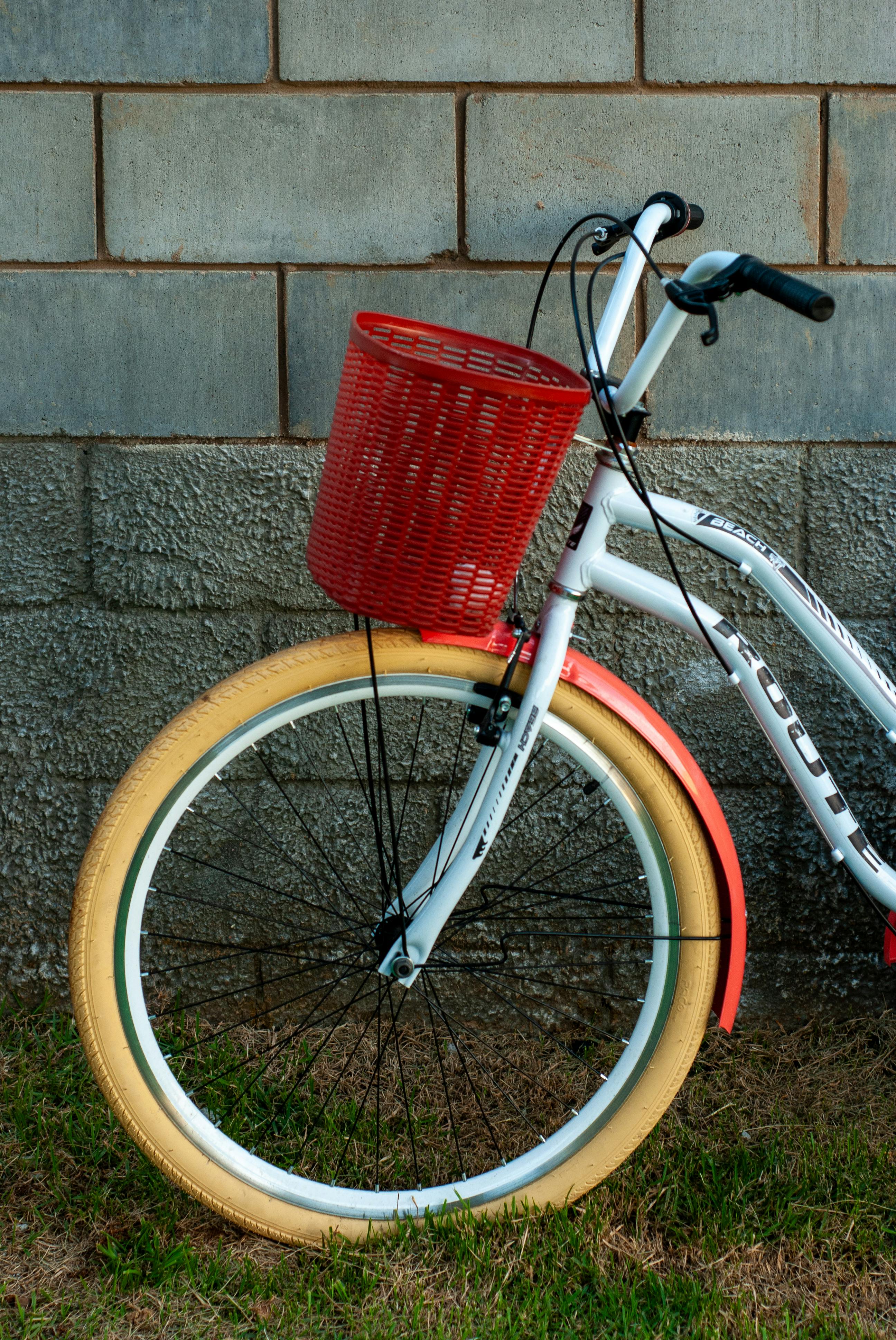 Bezpłatne Zabytkowy rower w żywych kolorach i czerwonym koszyku zaparkowany przy ceglanym murze. Zdjęcie z galerii