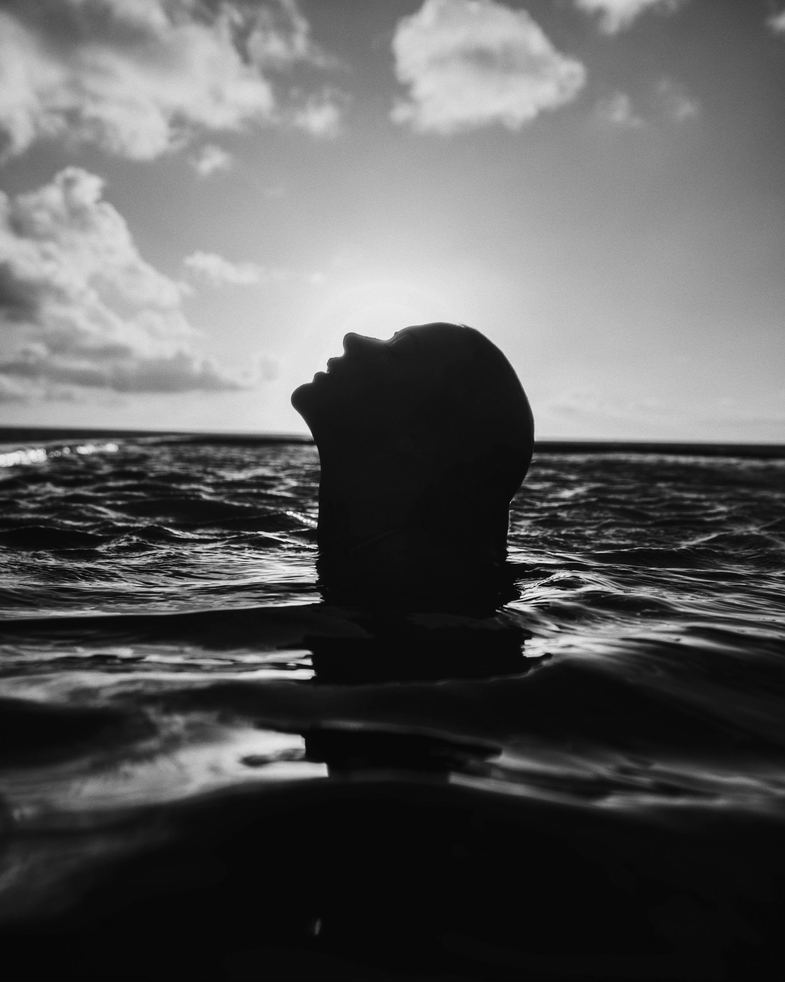 Bezpłatne Dramatyczna czarno-biała sylwetka człowieka w oceanie, uchwycająca spokój i wolność. Zdjęcie z galerii
