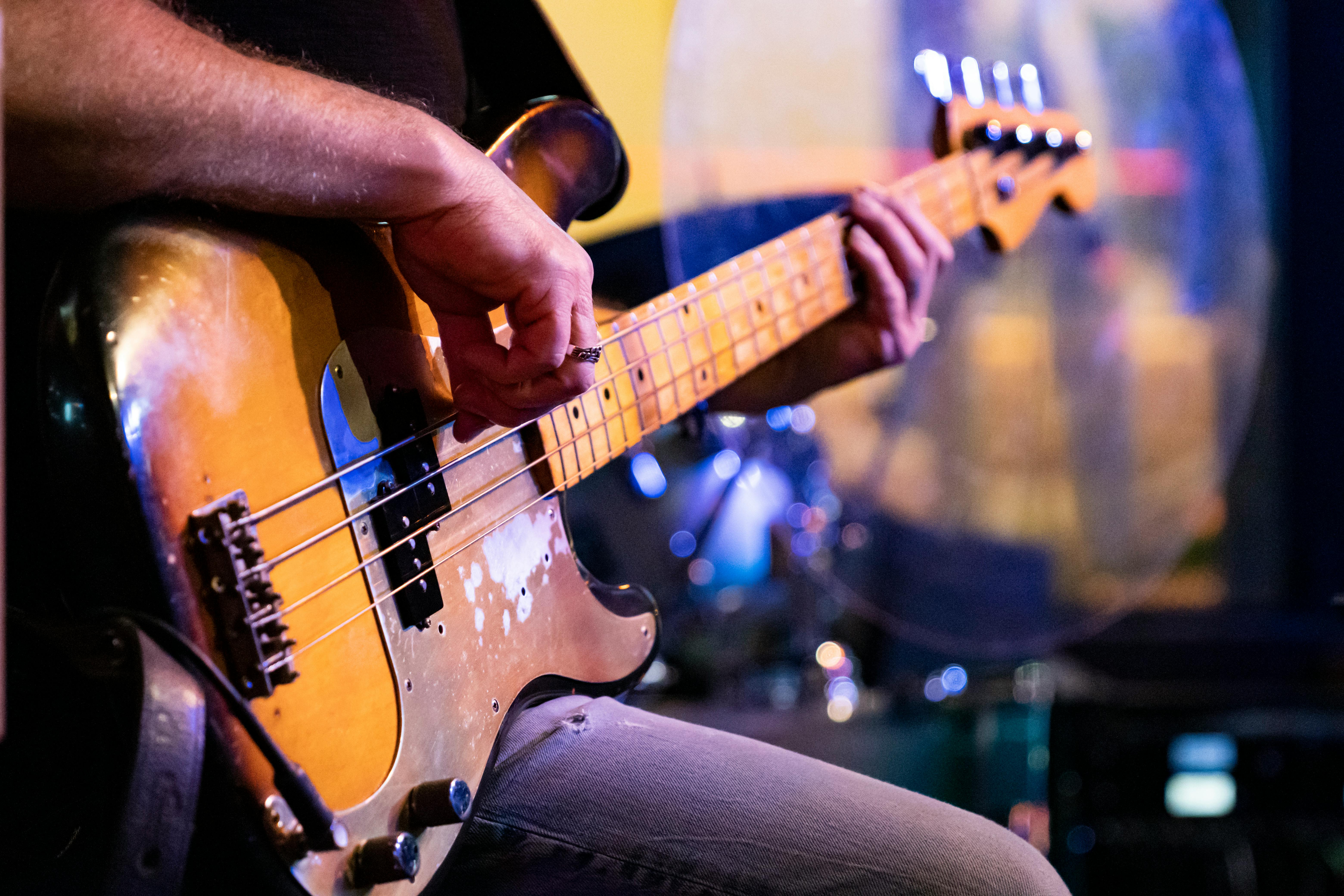 Gratis Tampilan detail jarak dekat seorang musisi yang memainkan gitar bass antik selama pertunjukan langsung. Foto Stok