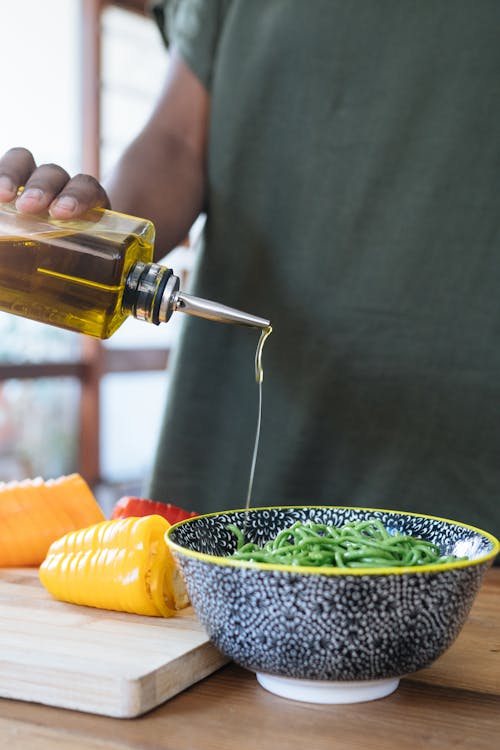 Free Person Pouring  Liquid on Green Noodles in Ceramic Bowl Stock Photo