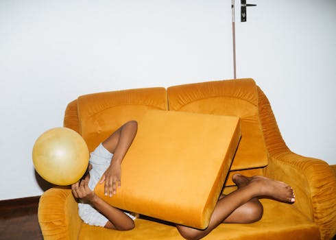 一个人开玩笑地放松在充满活力的黄色沙发上，手里拿着气球