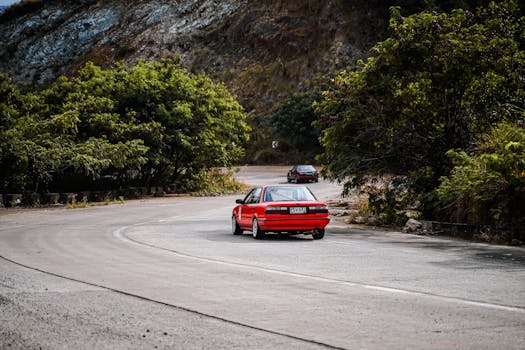 A red car driving on a scenic mountain road in Mangatarem, Philippines, surrounded by greenery and hills.