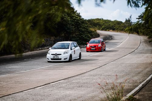 Free White and red cars navigate a scenic curved road in Mangatarem, Philippines. Stock Photo