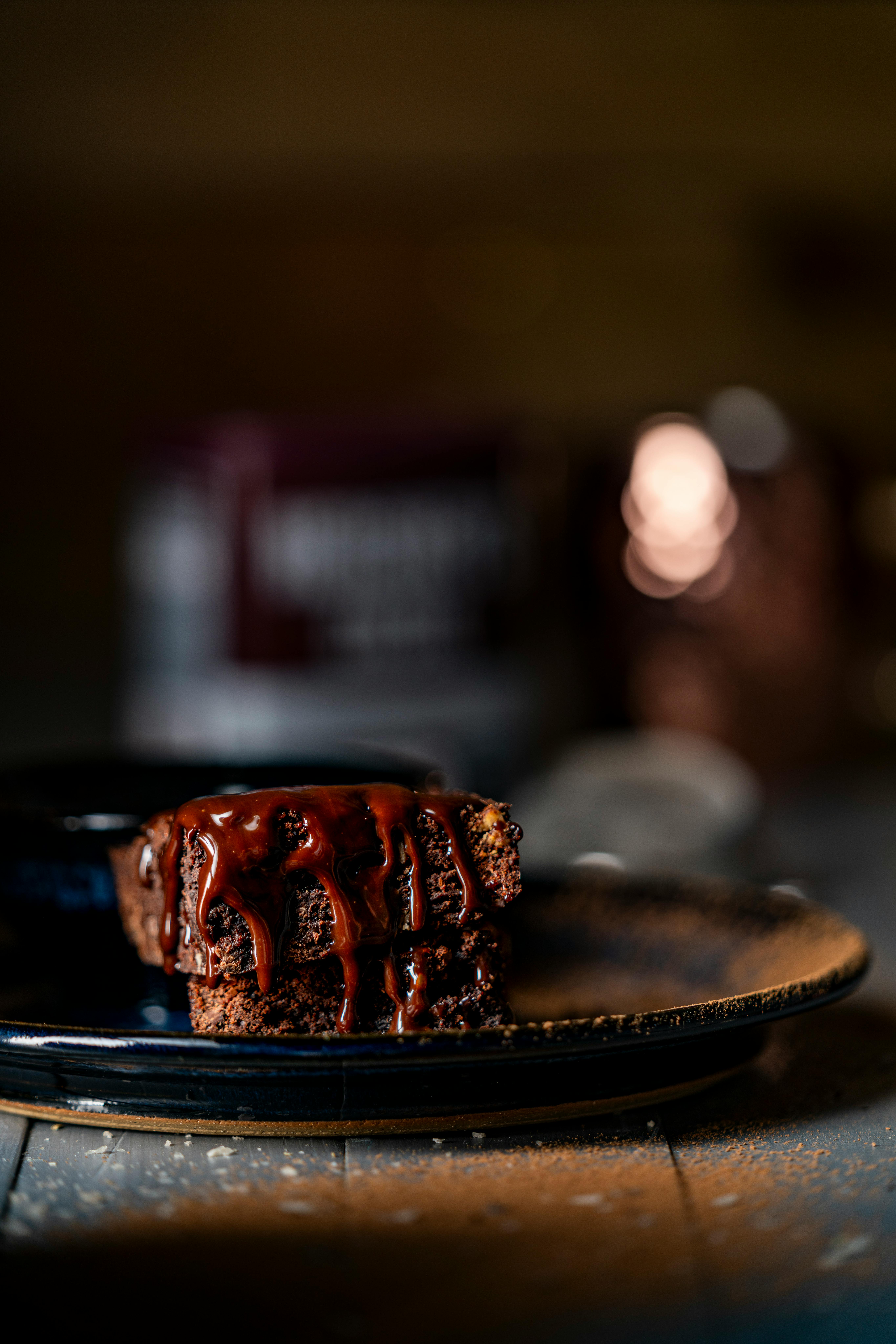 Close-up of a luscious chocolate cake drizzled with rich chocolate syrup on a dark plate, emphasizing indulgence.