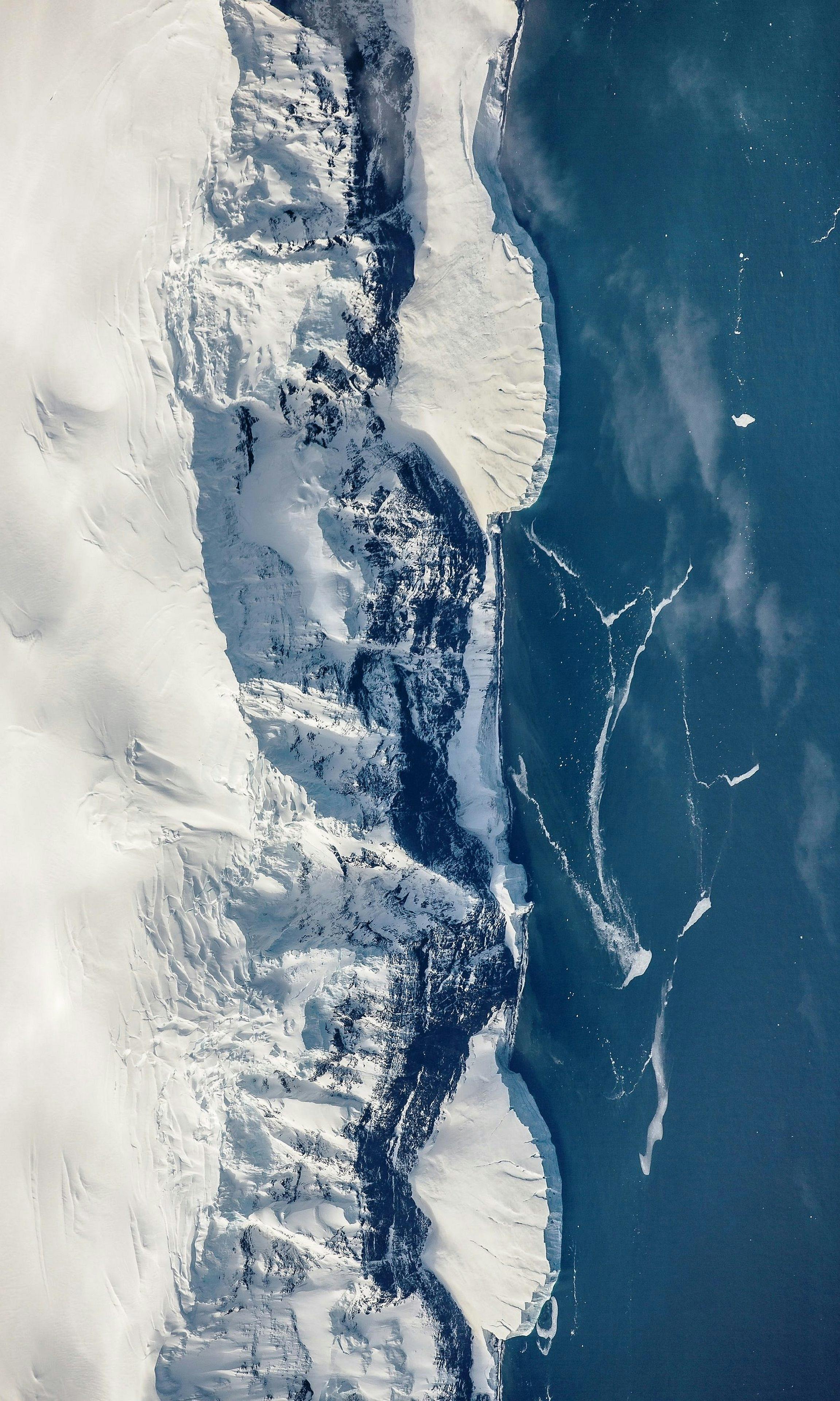 Majestic aerial view of a snowy coastline meeting icy waters, showcasing nature's frozen beauty.