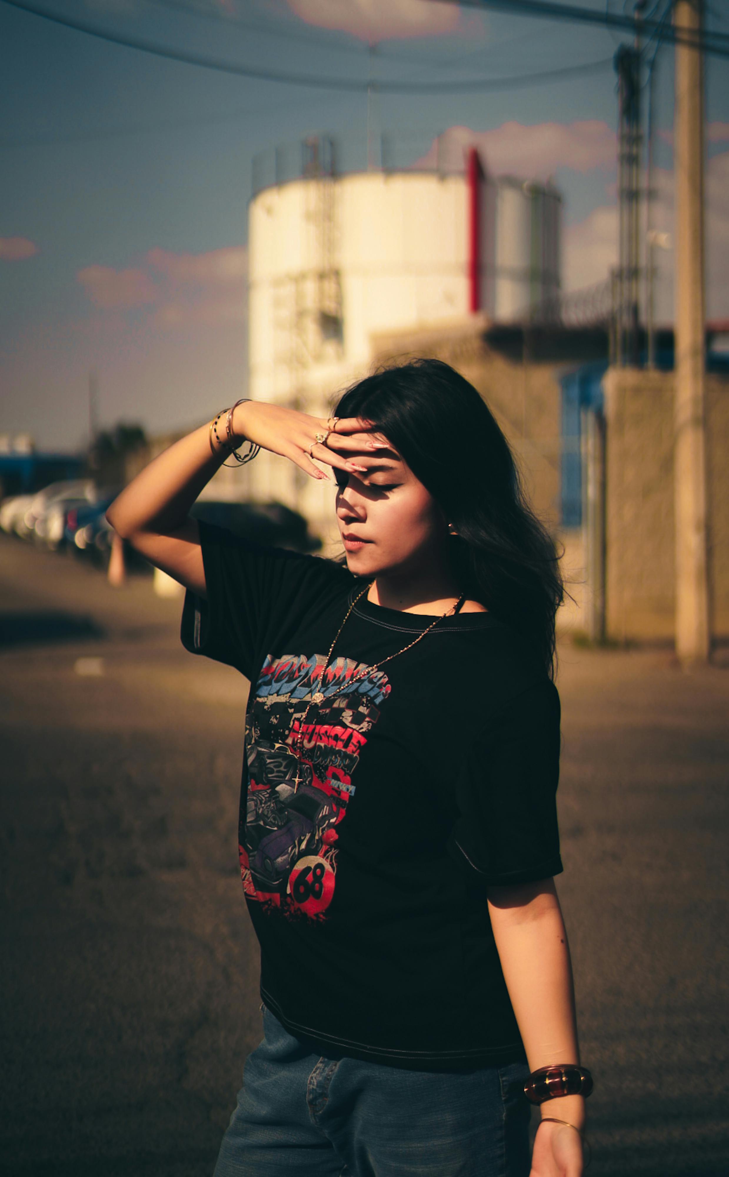 Bezpłatne Stylowa młoda kobieta osłaniająca oczy przed ciepłym słońcem na tle industrialnego krajobrazu. Zdjęcie z galerii