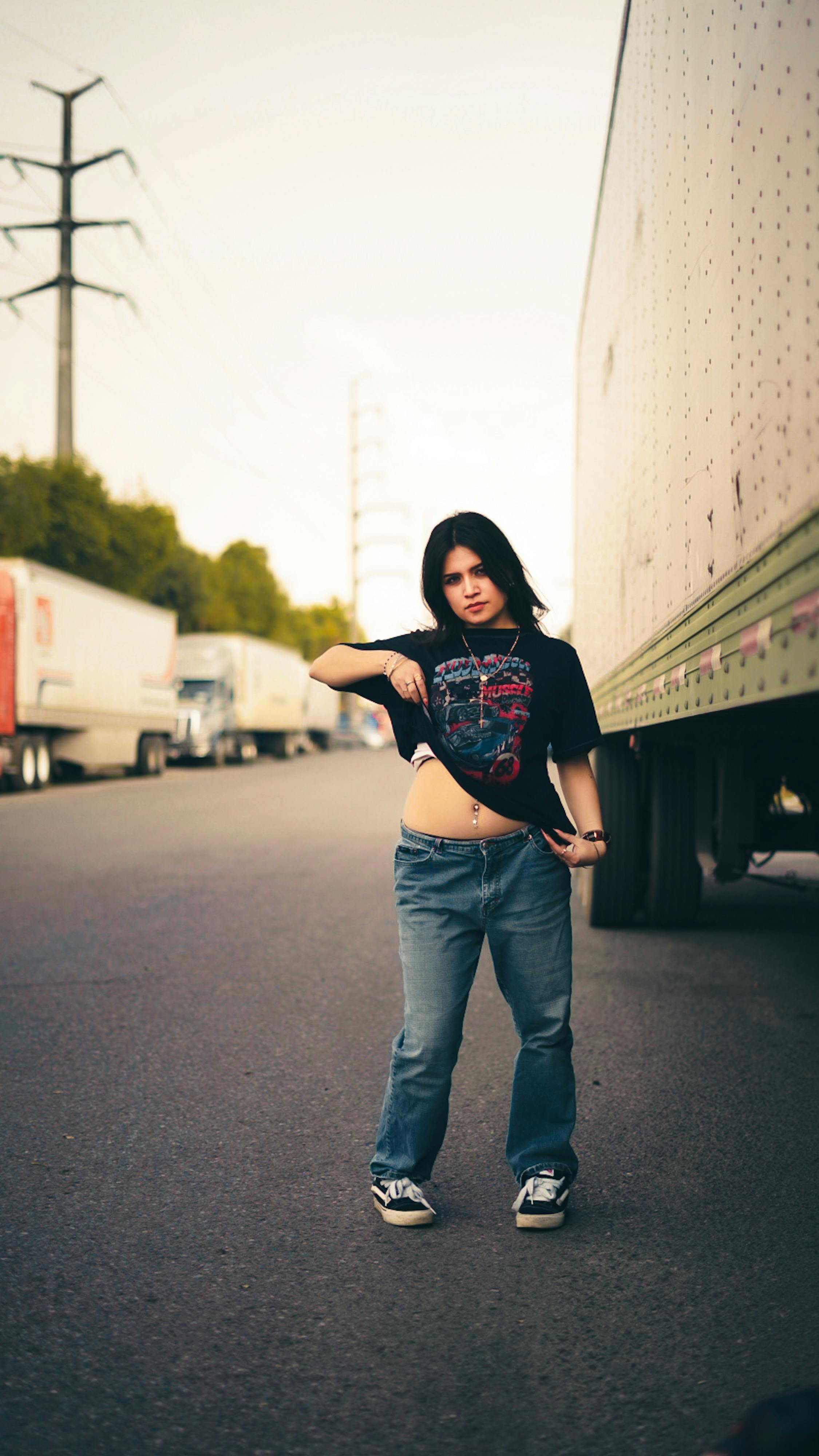 Bezpłatne Młoda kobieta pewnie pozuje obok ciężarówki na miejskiej ulicy, prezentując modny, swobodny ubiór. Zdjęcie z galerii