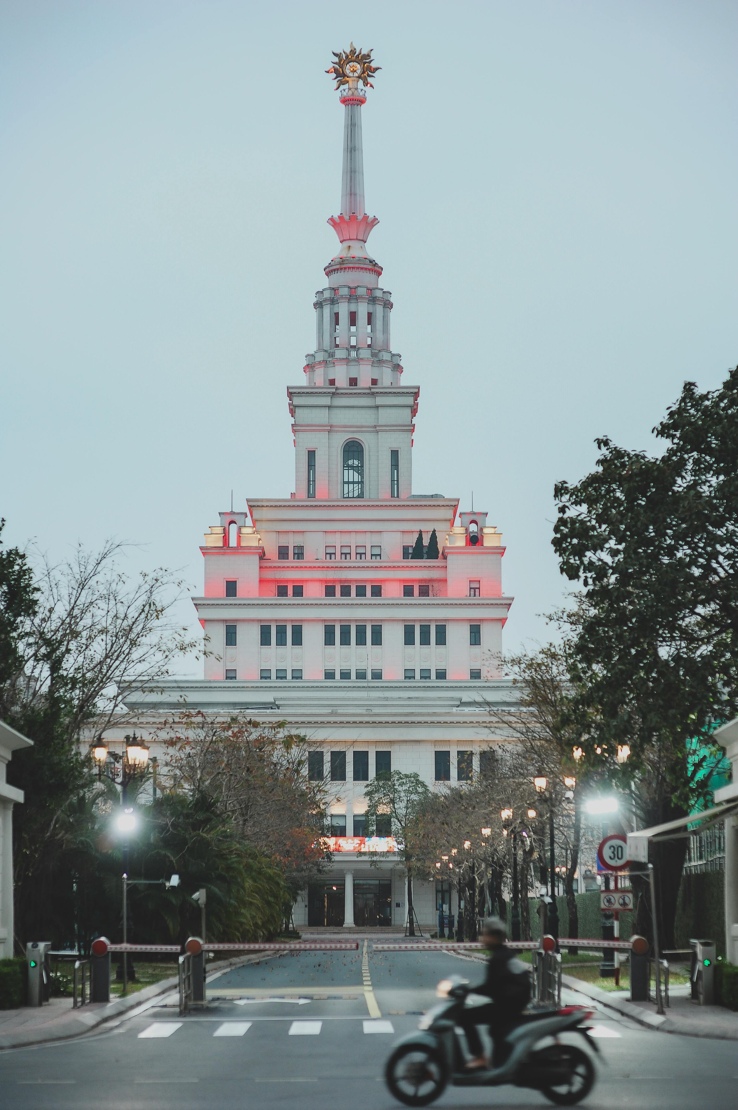 Gratis Menara bercahaya dengan desain arsitektur unik dan pengendara sepeda motor yang lewat saat senja. Foto Stok