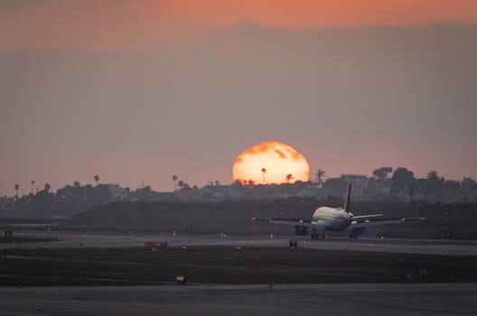 Airplane landing on LAX runway during a vibrant sunset, with silhouette of cityscape.
