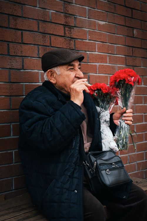 Free Senior man with bouquet of red flowers sits against a brick wall in Ankara, Türkiye. Stock Photo