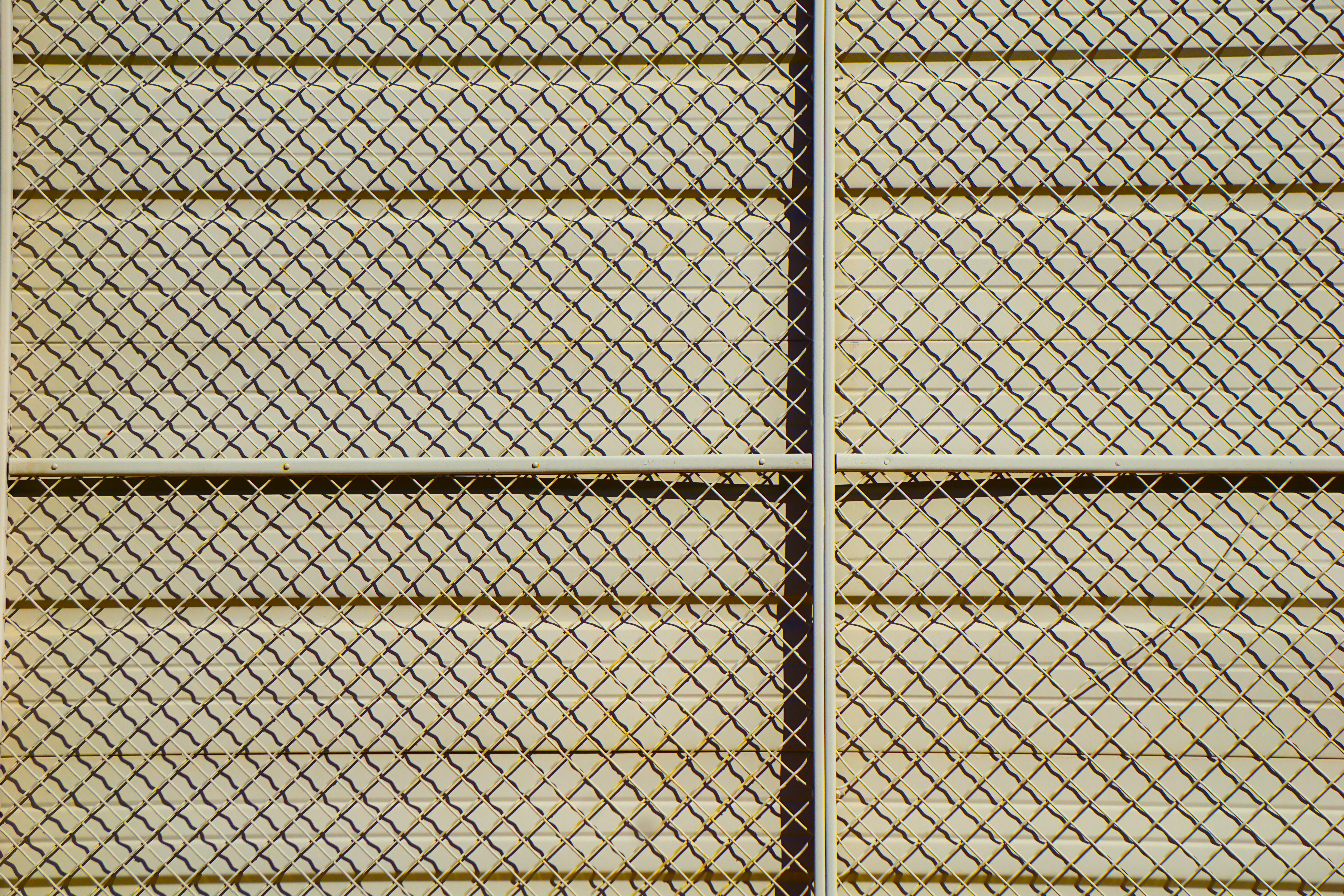 gratis Gedetailleerd patroon van een gaashekwerk dat schaduwen werpt en een gestructureerd rastereffect creëert. Stockfoto