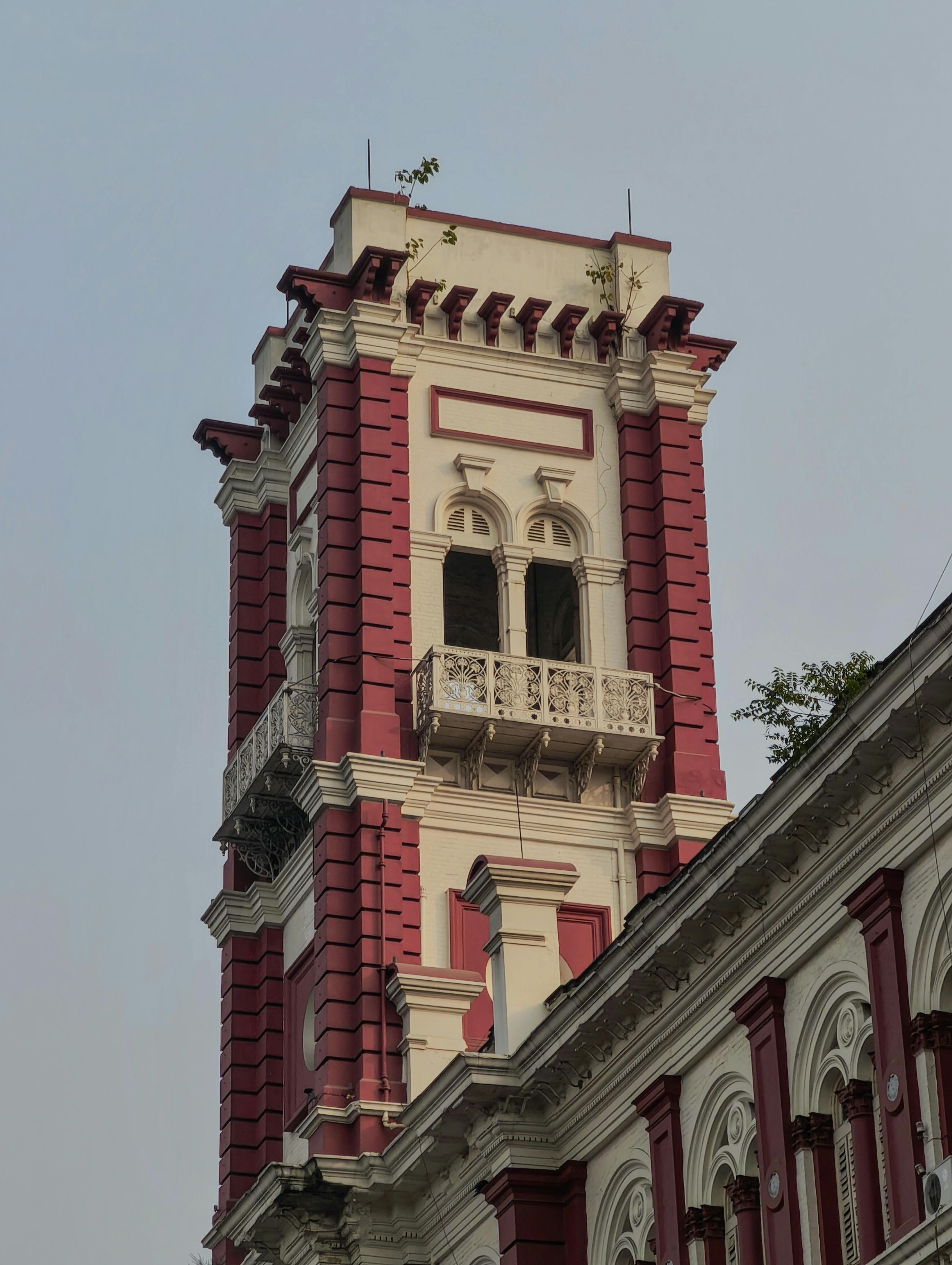 Gratis Primo piano di una storica torre dell'orologio rossa e bianca con archi decorati e cielo terso sullo sfondo. Foto a disposizione