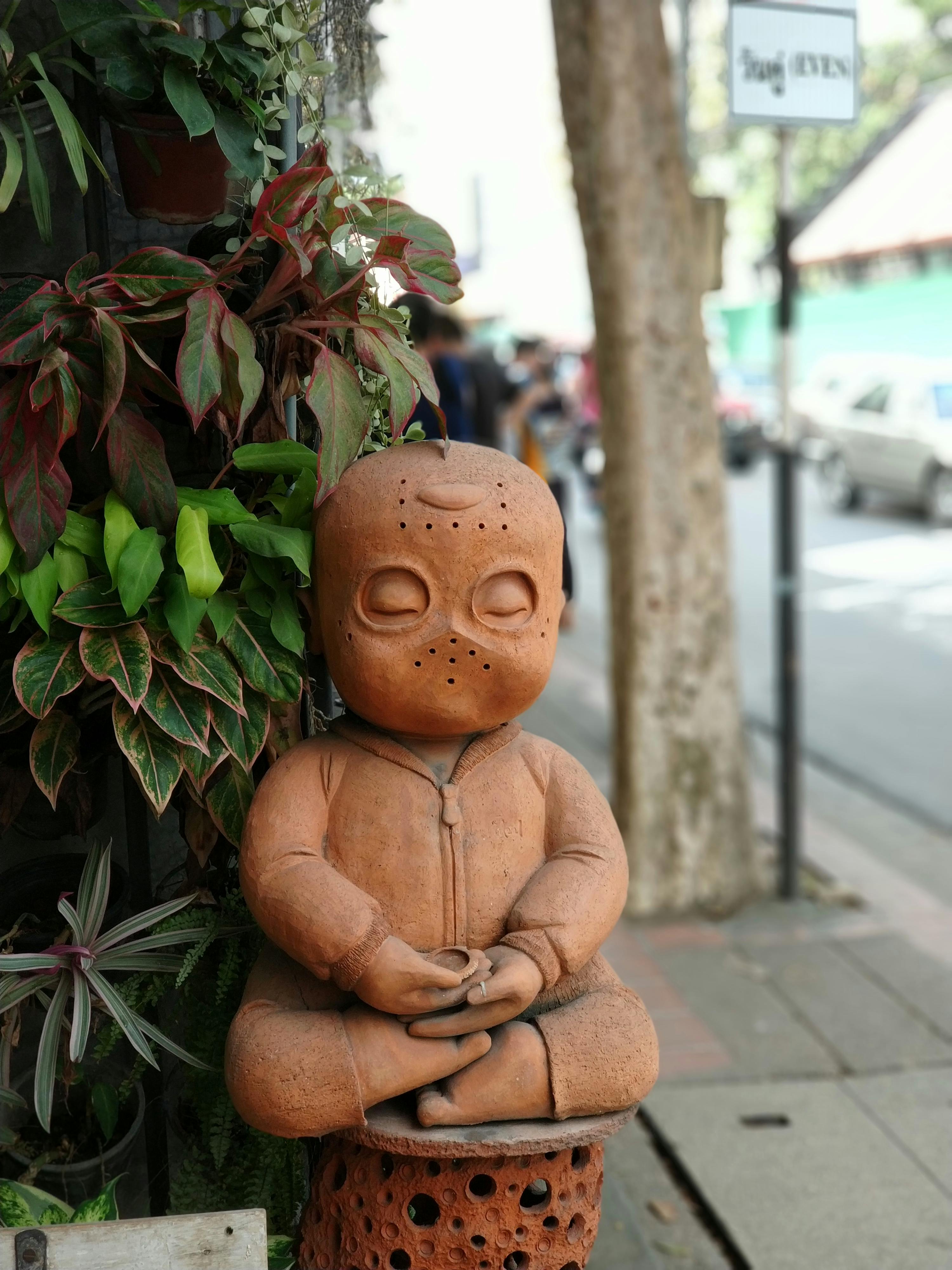 Gratuit Statuie de lut în poză meditativă pe fundalul unui trotuar urban cu frunziș vibrant. Fotografie de stoc