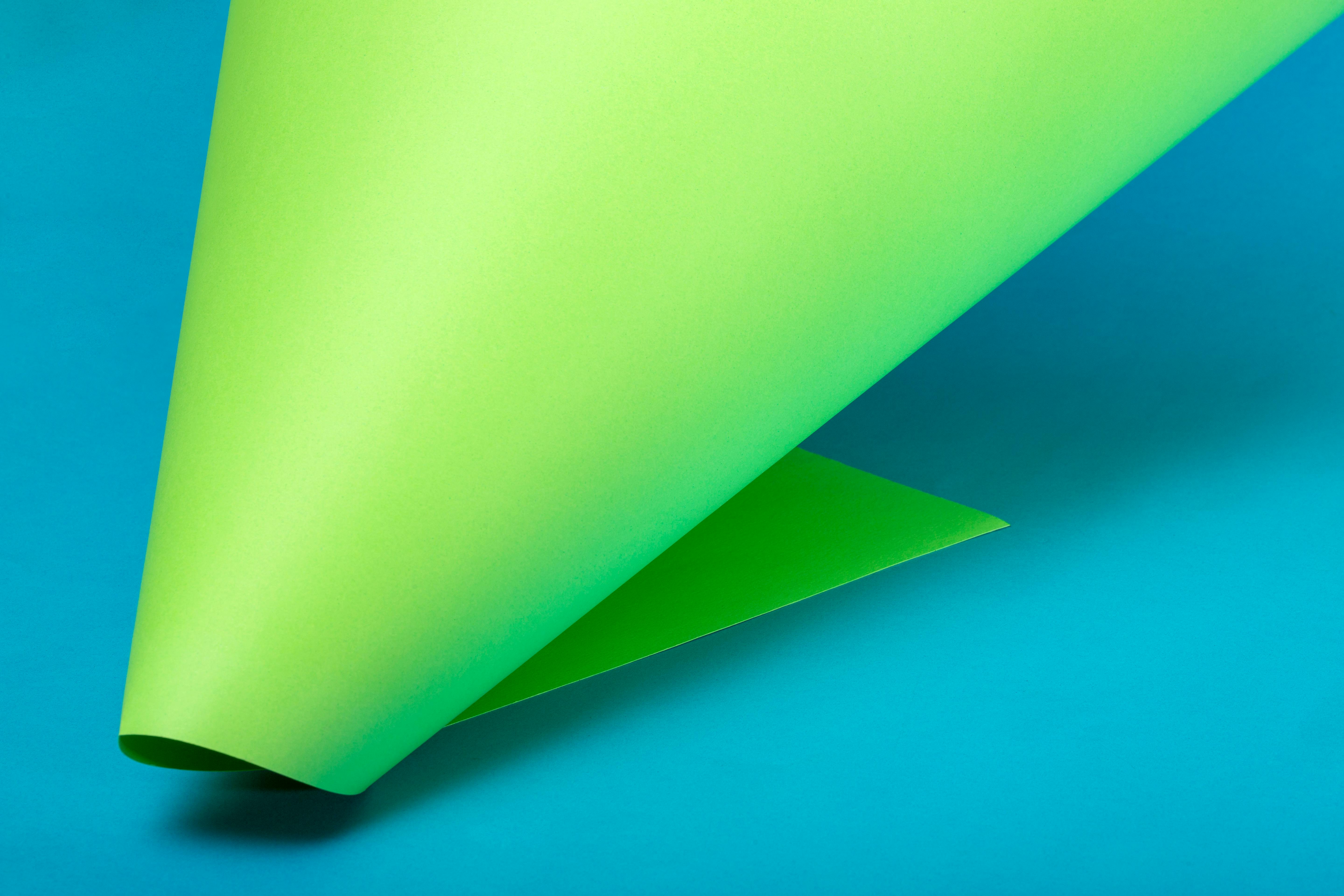 Kostenlos Ein abstraktes Kunstwerk, das ein leuchtend grünes, über einen hellblauen Hintergrund gerolltes Papier zeigt. Stock-Foto