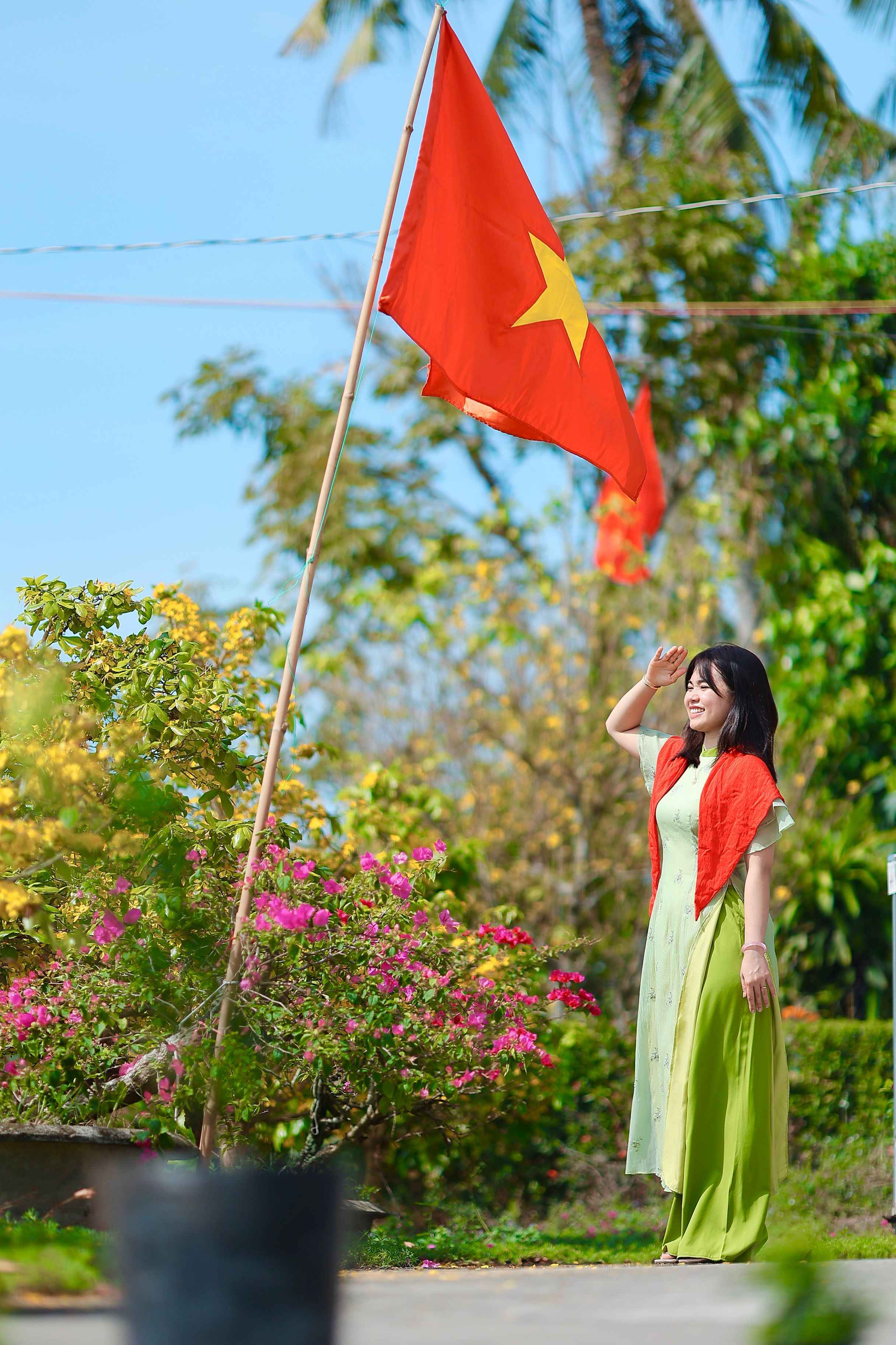Woman in traditional dress saluting under the Vietnamese flag outdoors.