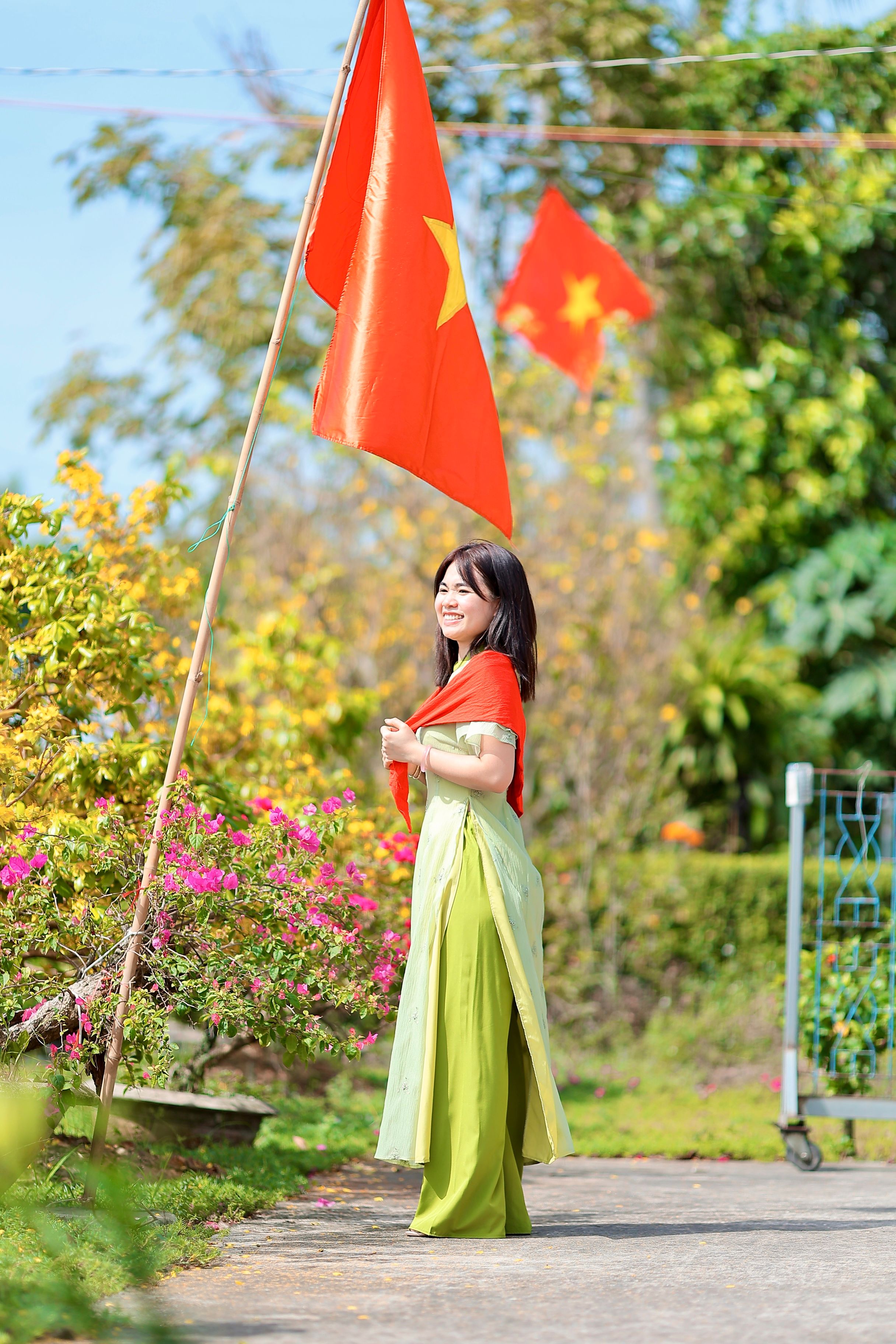 A woman poses in traditional attire with flags in a bright, outdoor setting.