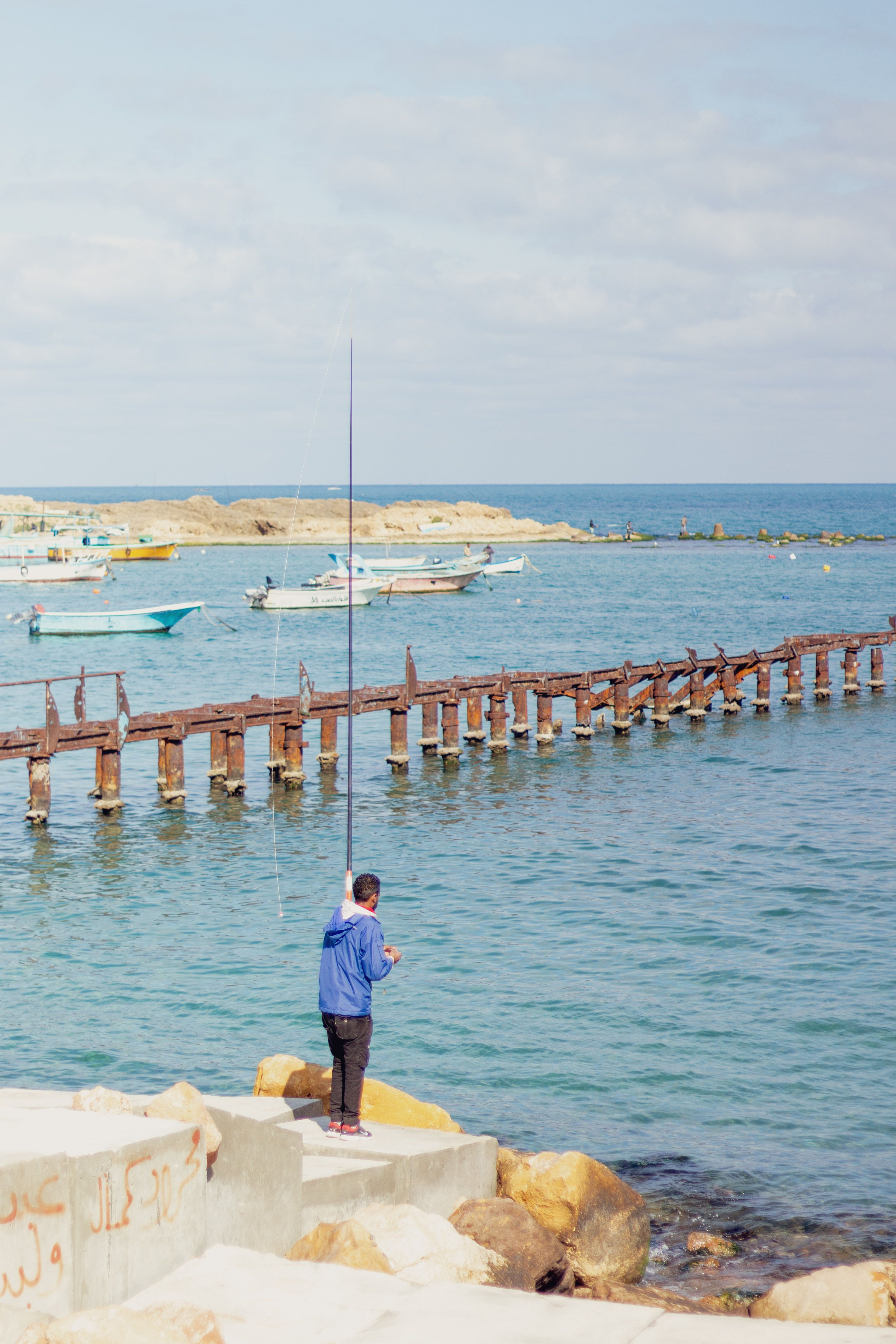 Gratis Un pescador solitario en un viejo muelle en Alejandría, Egipto, durante una serena puesta de sol. Foto de stock