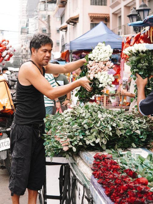 Free A vendor arranges vibrant flowers at a bustling outdoor market, showcasing a variety of blooms. Stock Photo