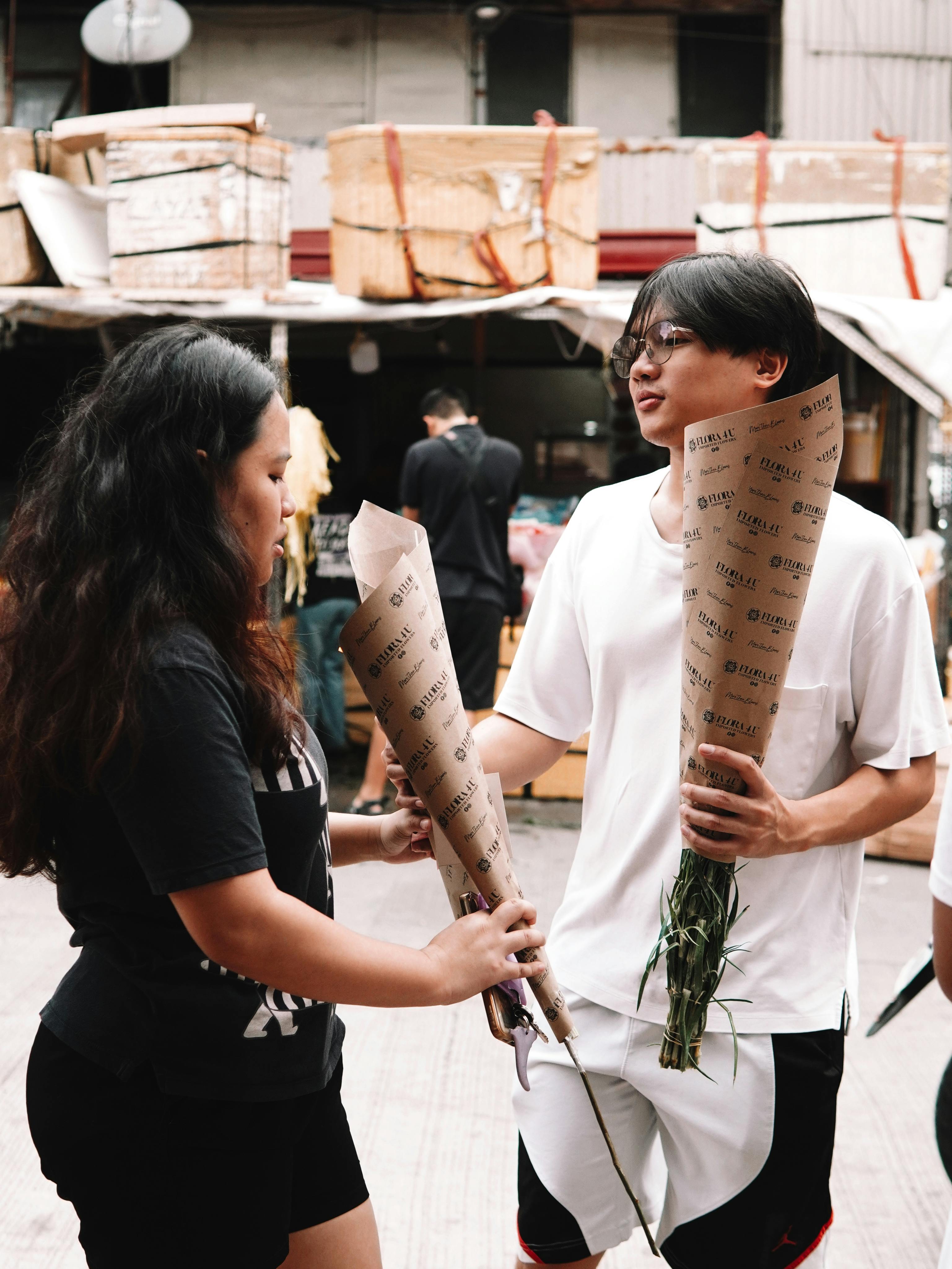 Gratis To unge voksne udveksler blomster på et travlt marked. Lagerfoto