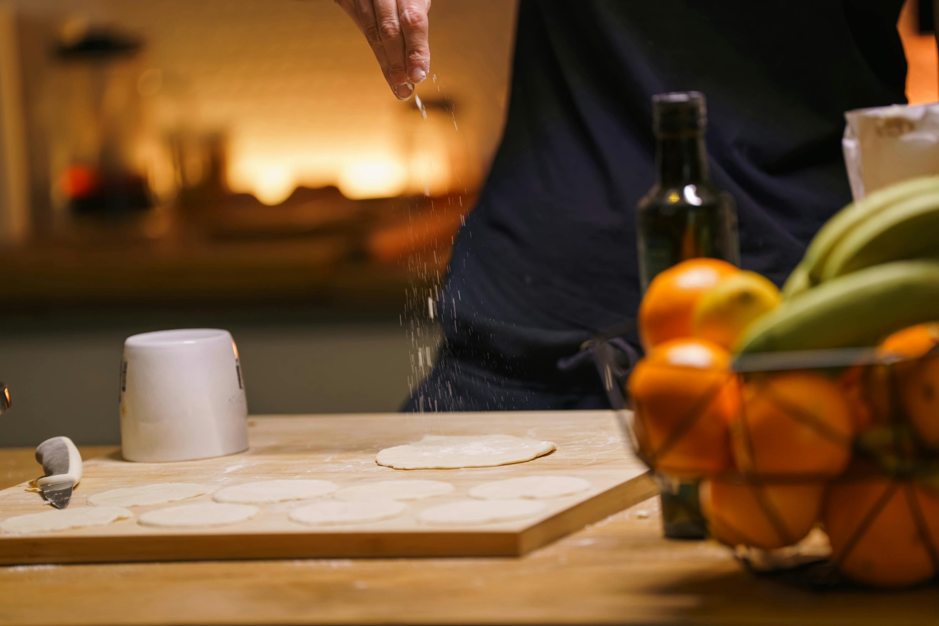 Gratis Varmt og indbydende køkken med meldryssede hænder, der tilbereder dej, omgivet af frisk frugt. Lagerfoto