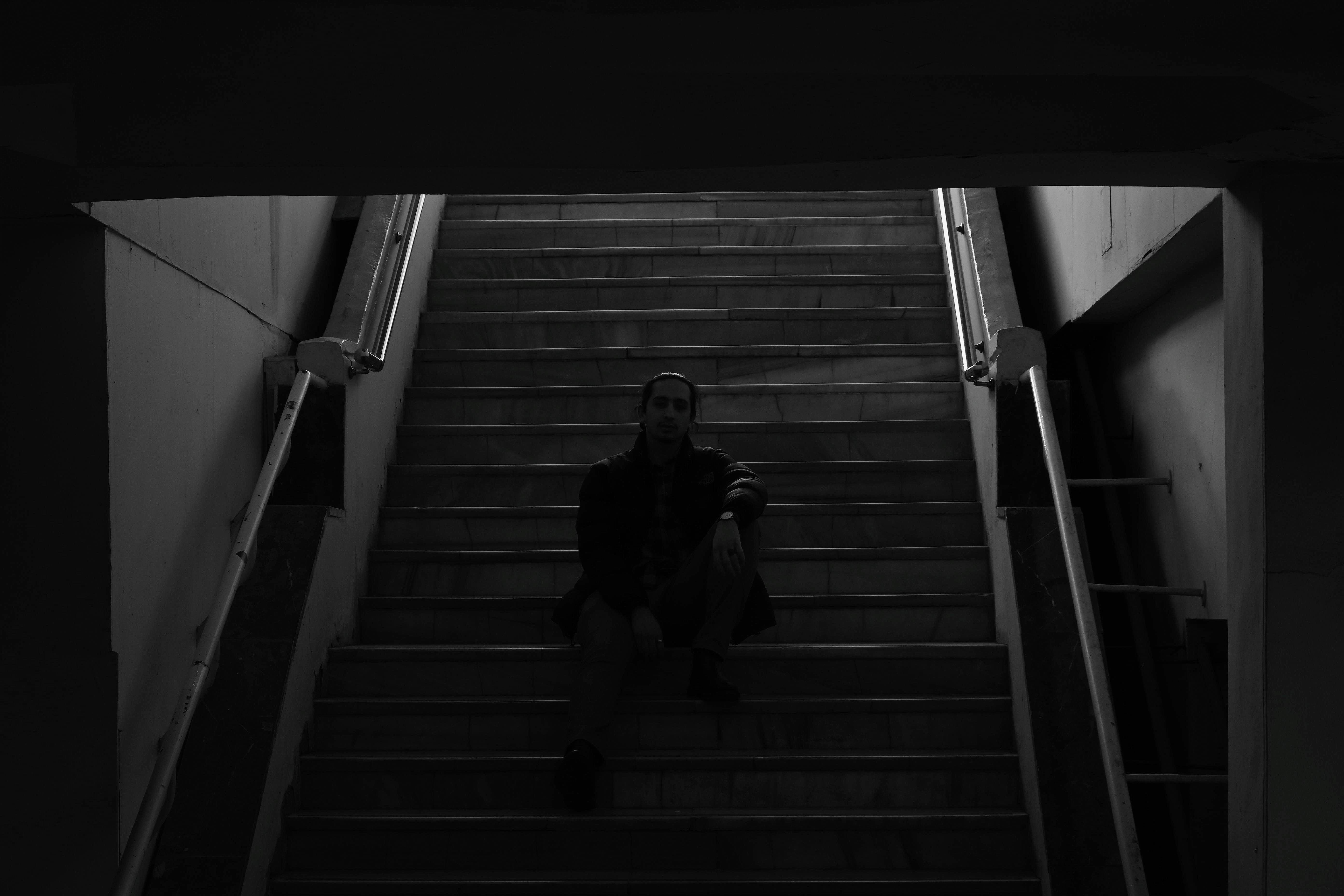 grátis Uma pessoa solitária senta-se numa escadaria escura, evocando solidão e introspecção. Foto profissional