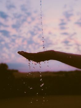 Hand catching water in silhouette against a beautiful sunset sky, evoking calm and serenity.
