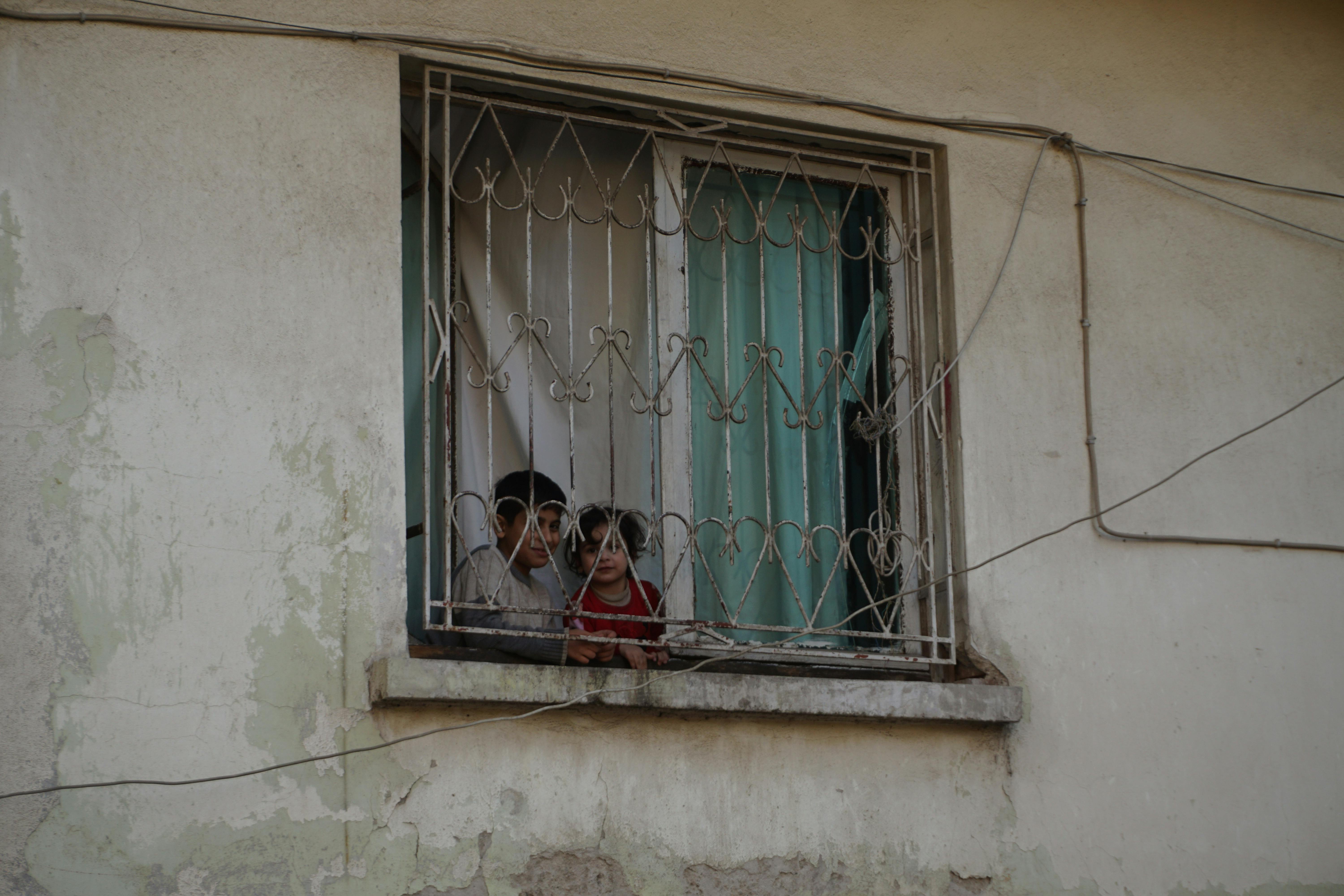 Gratis To barn ser ut av et gittervindu og fanger et øyeblikk av nysgjerrighet og ettertanke. Arkivbilde