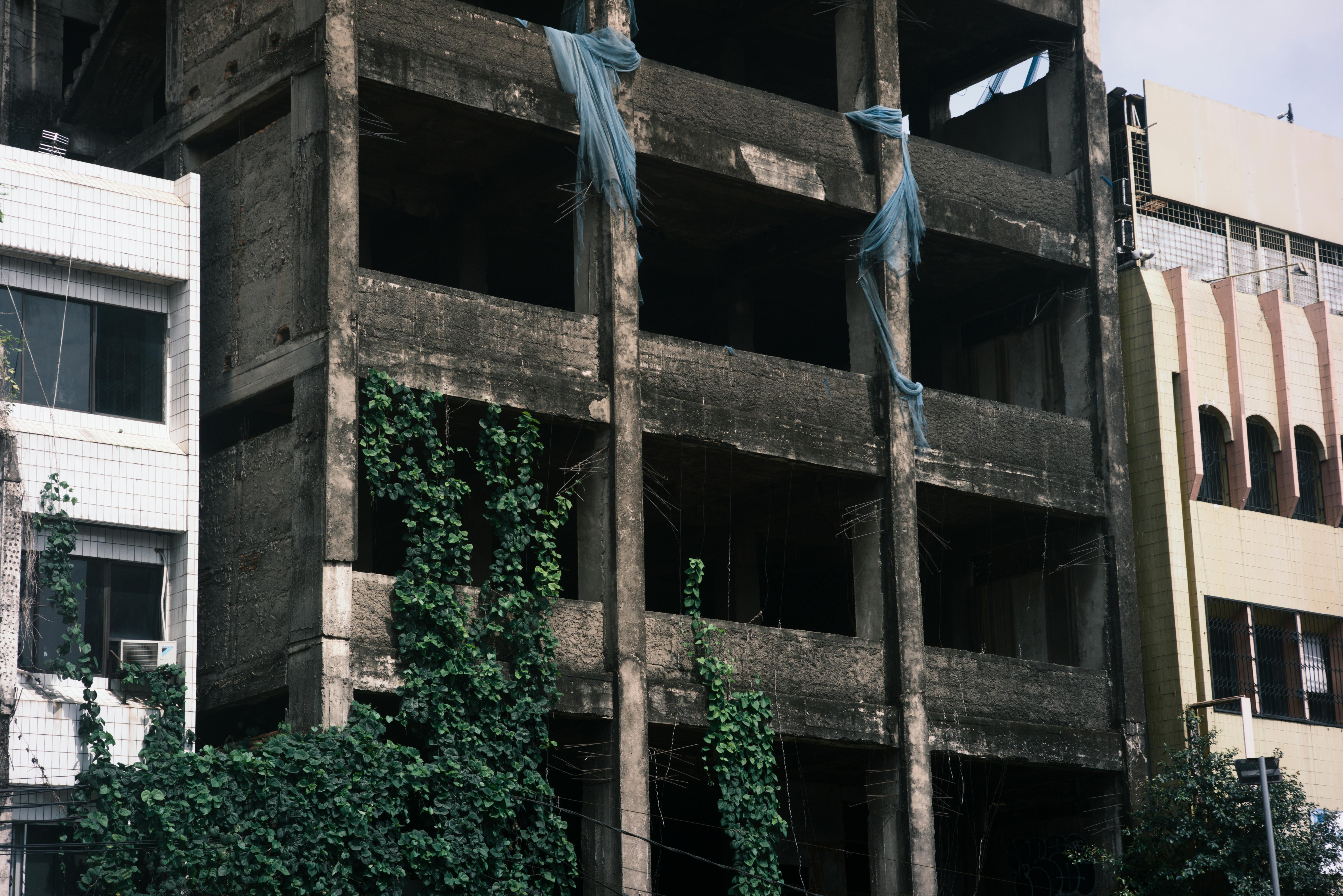 Bezpłatne Rozpadający się, niedokończony budynek porośnięty przerośniętą roślinnością w miejskim otoczeniu. Zdjęcie z galerii